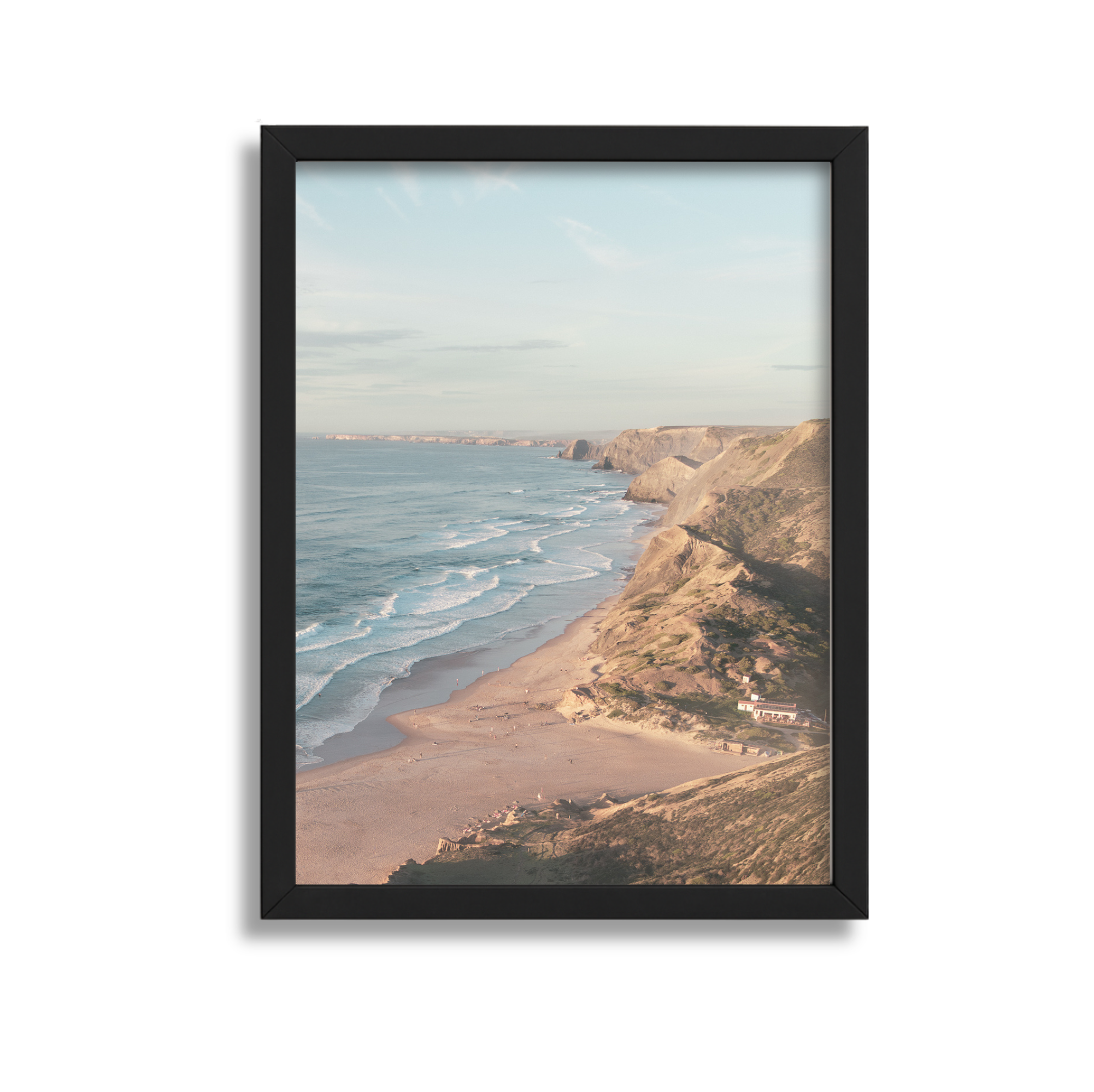 Framed photograph of a coastal landscape with cliffs, sandy beach, ocean waves, and partly cloudy sky.