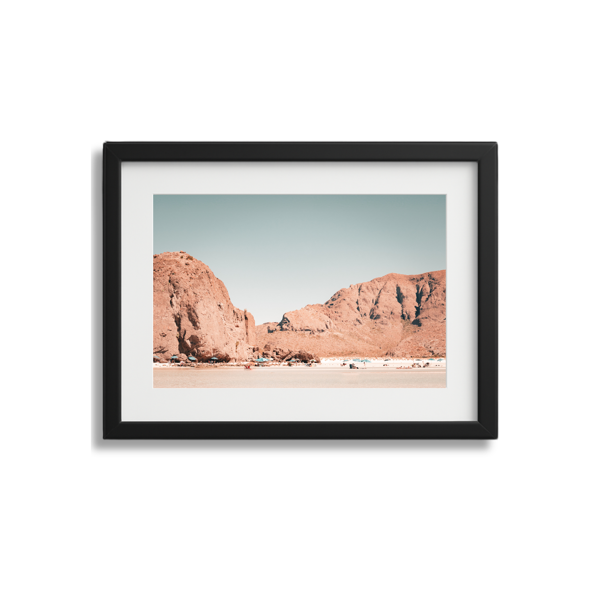 Photograph of desert landscape with large reddish-brown rocky formations and a flat sandy foreground, under a clear sky.
