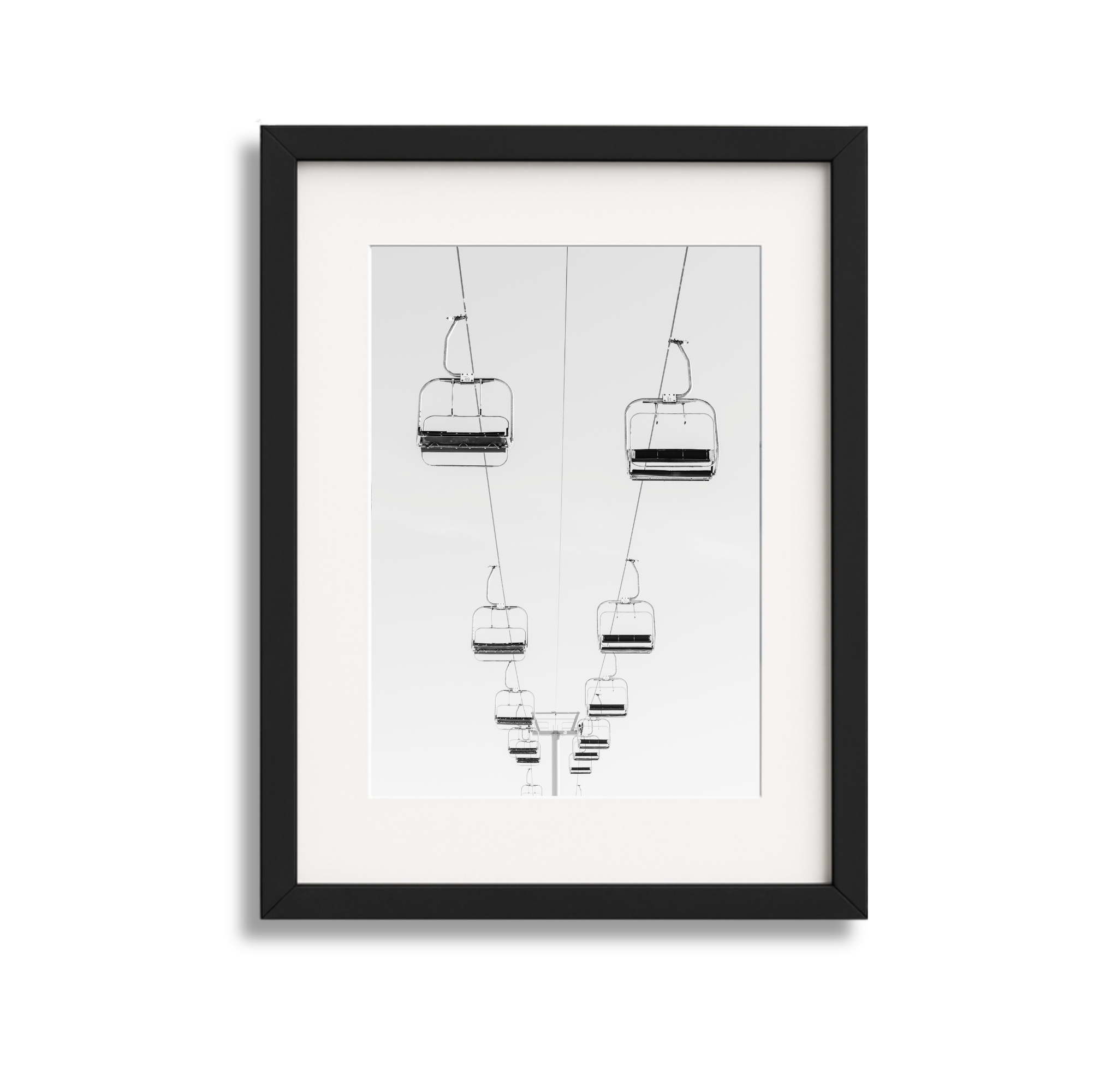 Black and white framed photograph of ski lift chairs hanging from cables, perspective from below.