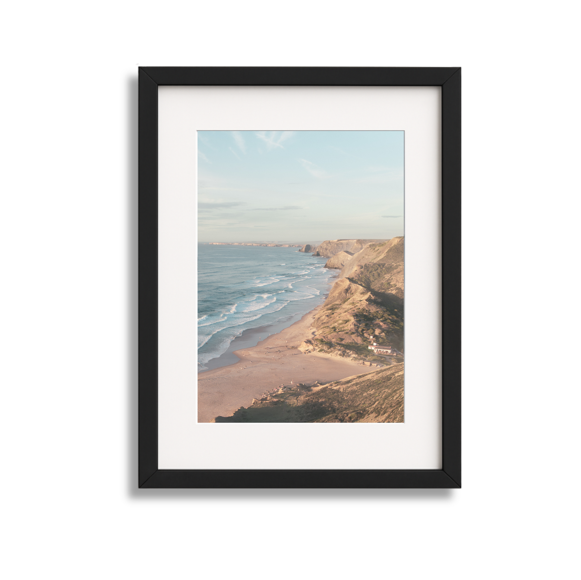 Framed photograph of a coastal scene with cliffs, sandy beach, and ocean waves under a partly cloudy sky.