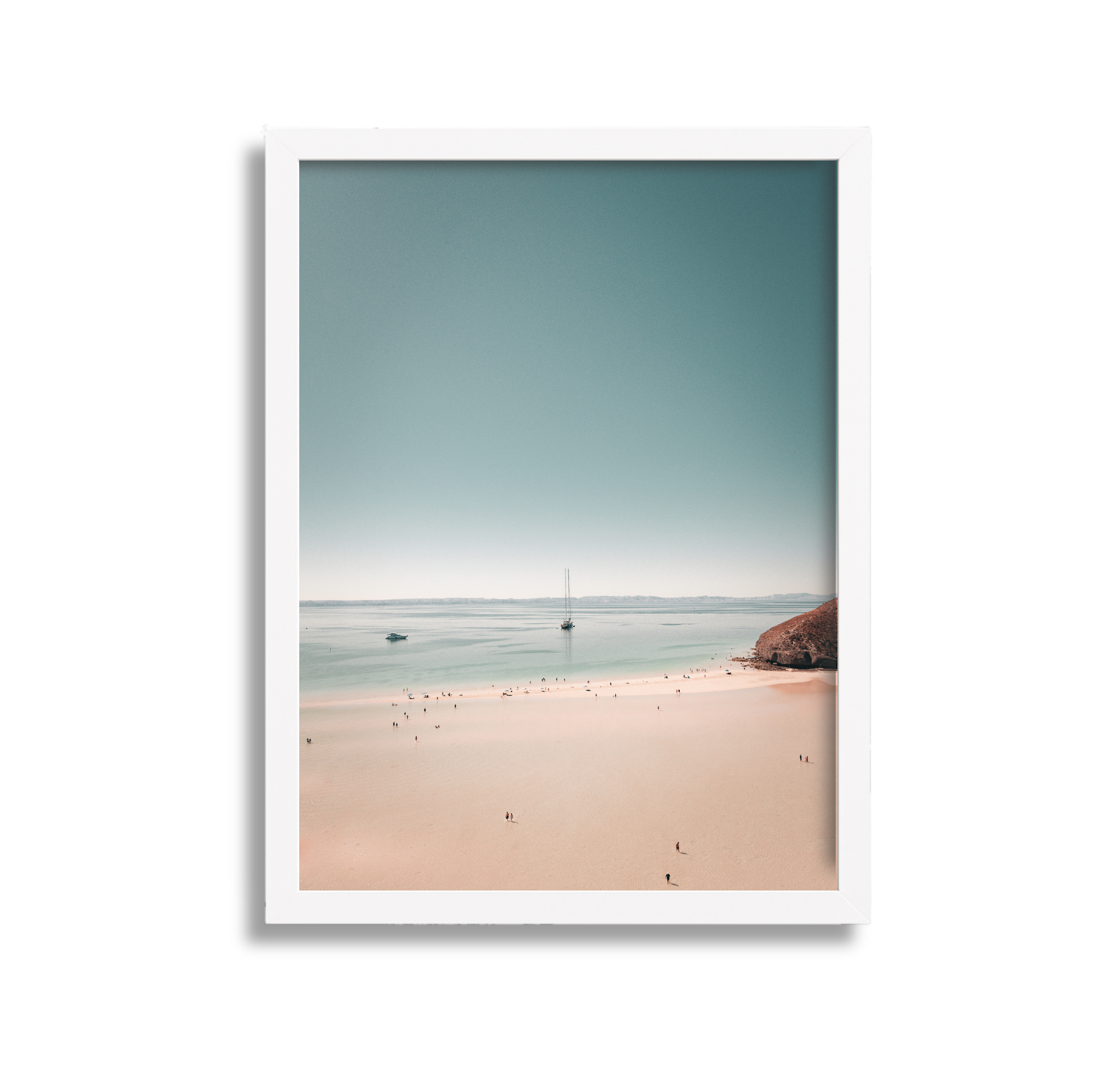A framed photograph of a beach scene with sand, water, and sailboats under a clear sky.