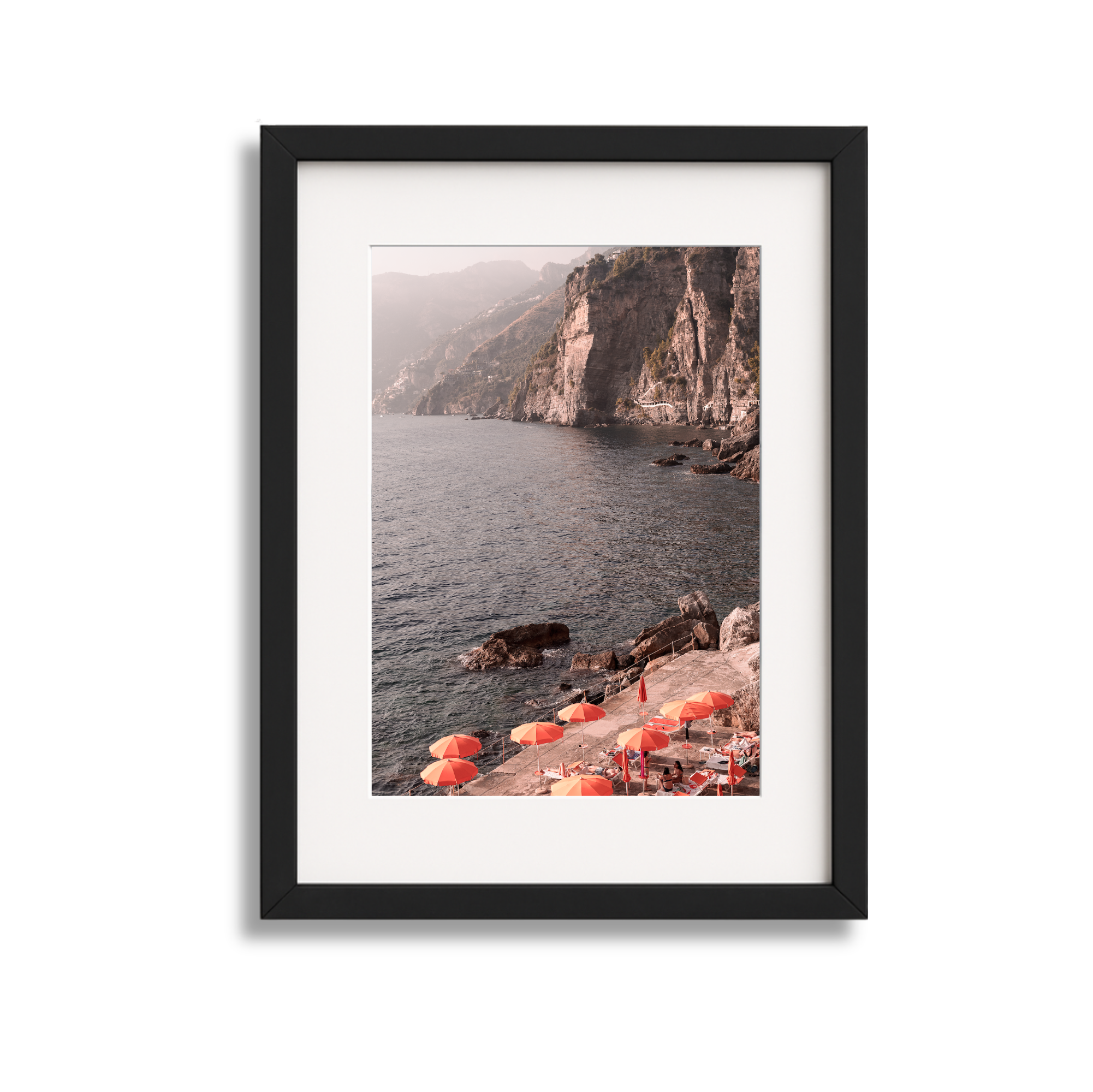 Photograph of a coastal scene with orange umbrellas and beach chairs on a rocky shoreline, with towering cliffs in the background and calm water in the foreground.