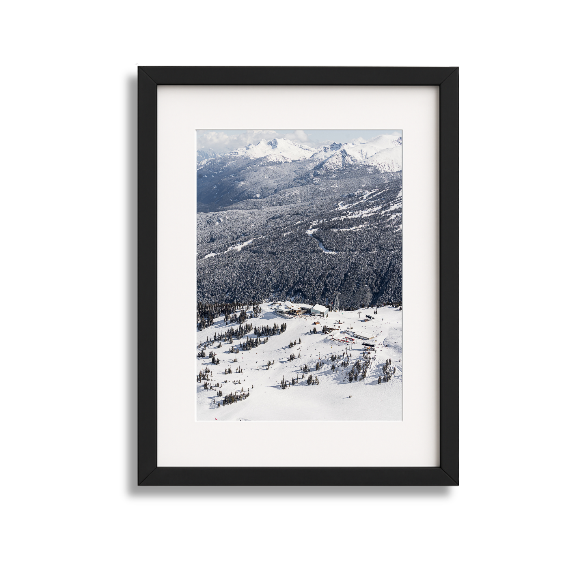 Framed aerial photograph of a snowy mountain landscape with ski resort buildings and trees.