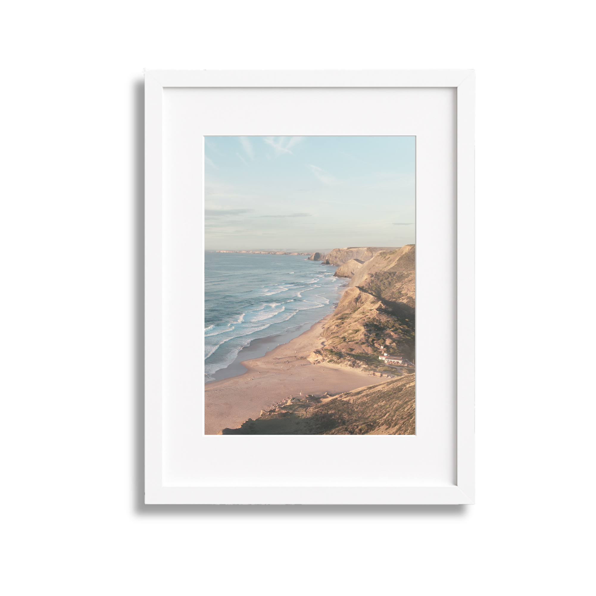 Framed photograph of a coastal landscape with cliffs, sandy beach, ocean waves, and partly cloudy sky.