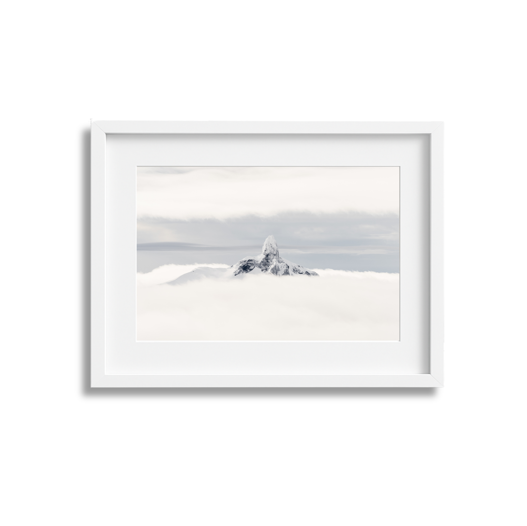 A framed photograph of a snow-capped mountain peak rising above clouds, with a cloudy sky in the background.