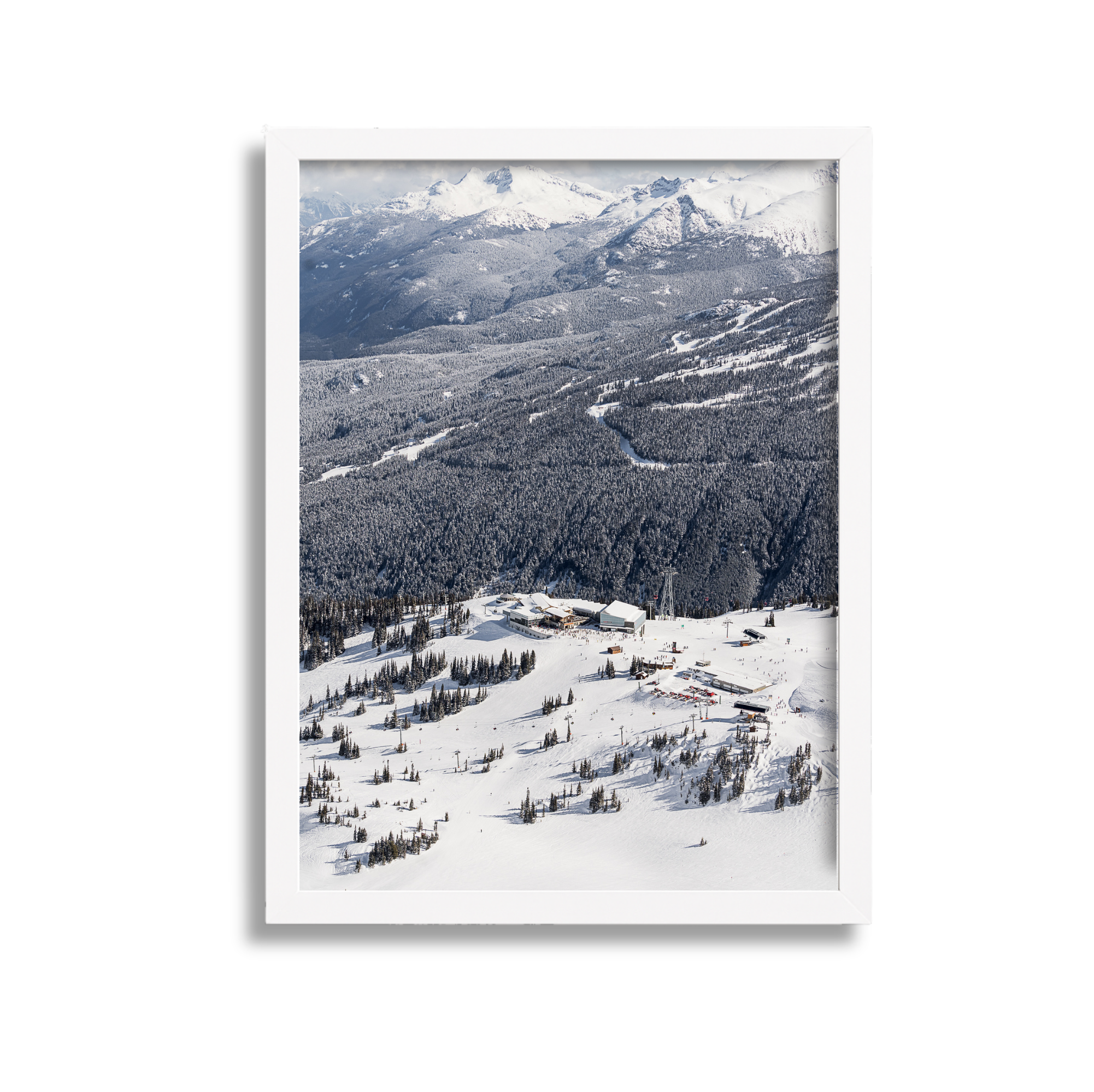 Snow-covered mountain landscape with ski resort buildings and trees in foreground and snow-capped mountains in background.