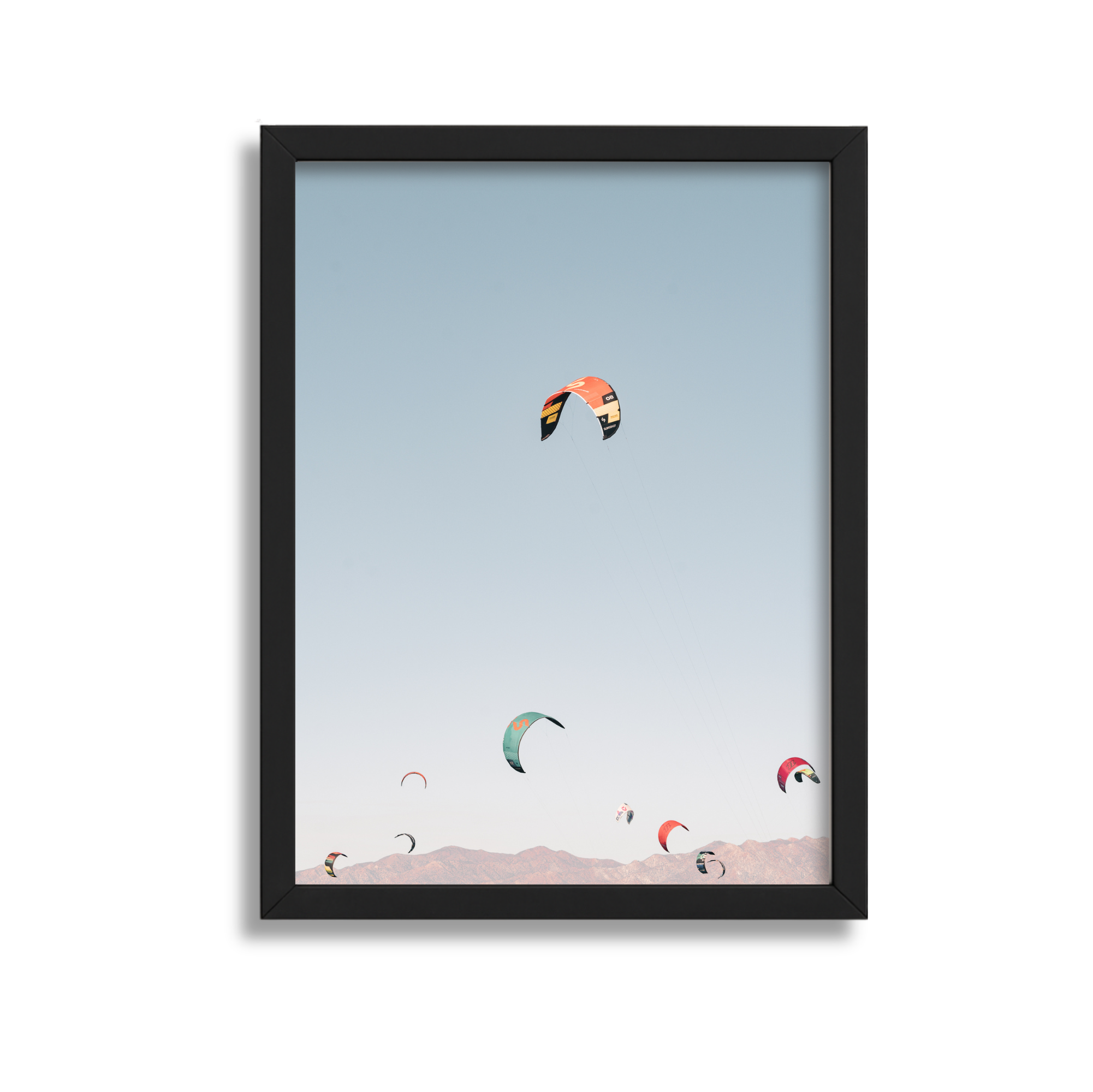 Framed photograph of multiple colorful kites soaring in the sky over mountain range.