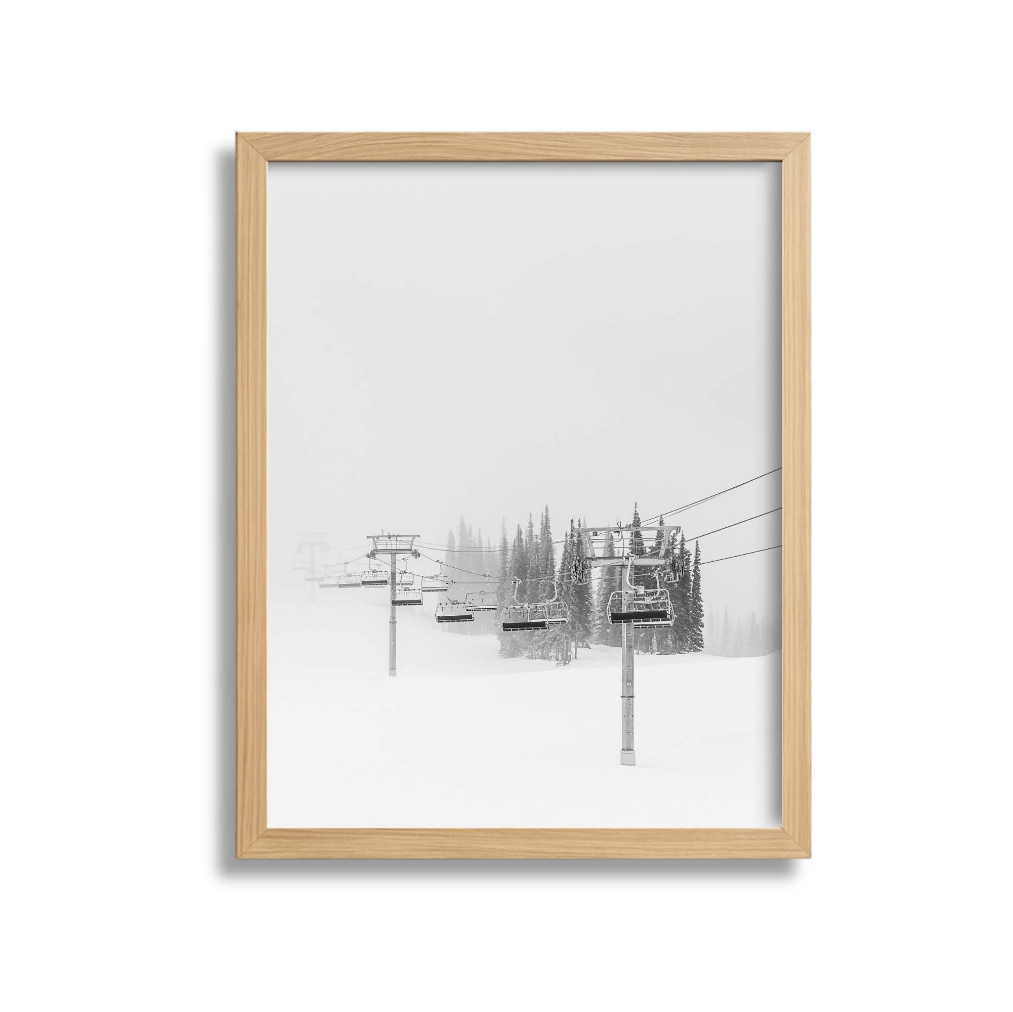 A black and white photo of a ski lift with empty chairs on snow-covered ground, trees, and fog in the background.
