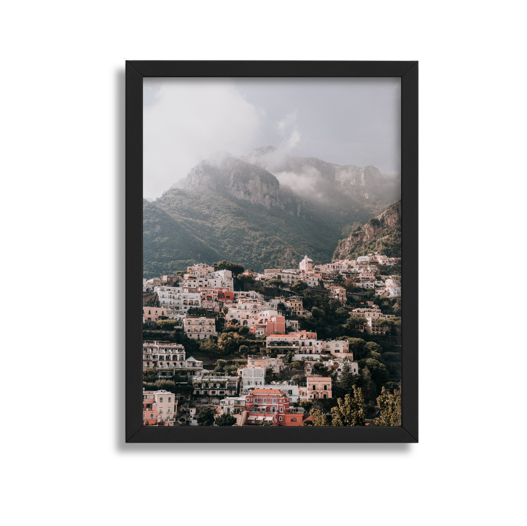 A large framed fine art photography print of scenic view of Positano Italy through a black picture frame, with mountains and cloudy sky in the background with a black frame. 
