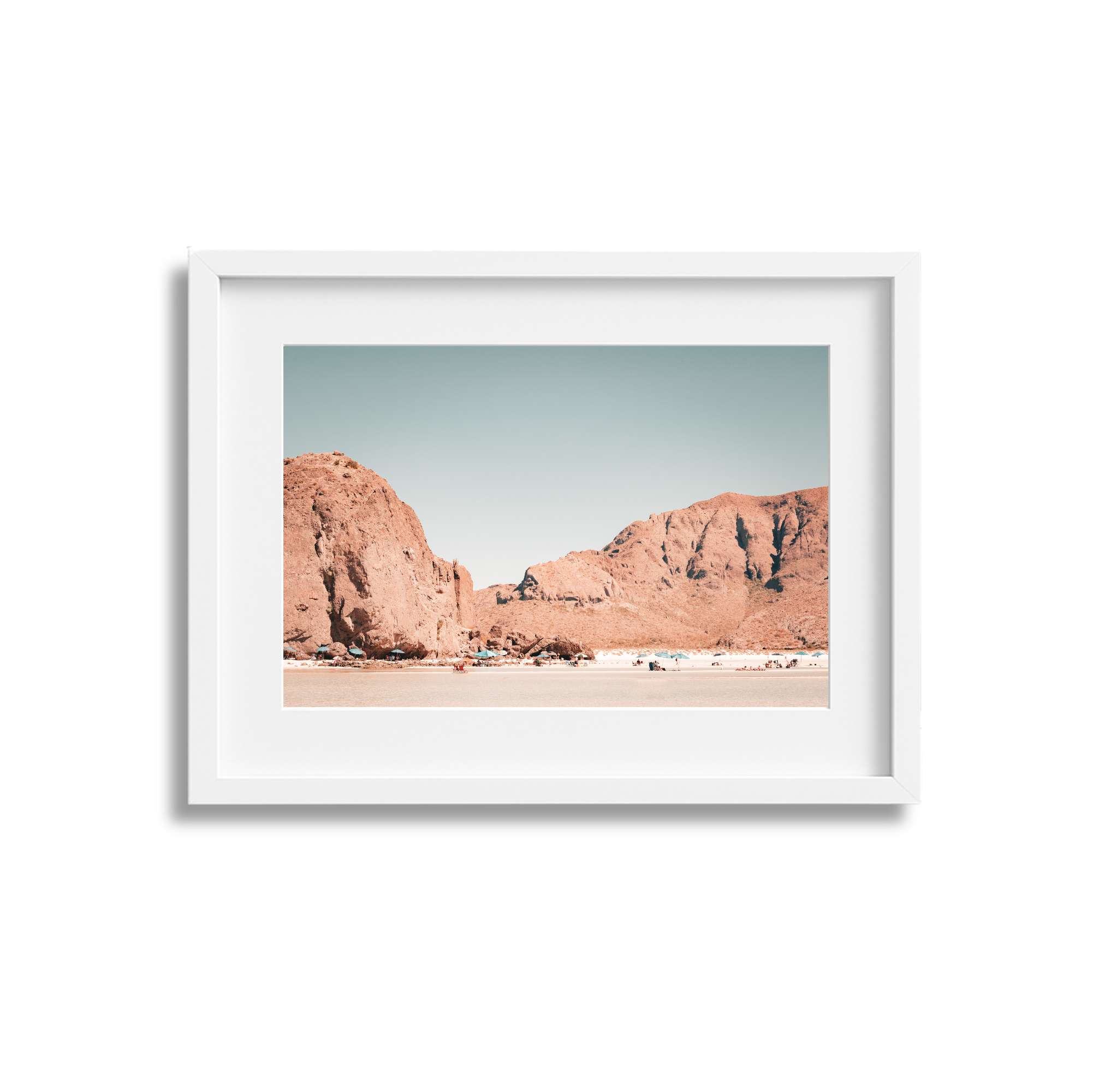 Framed photo of a desert landscape with large rock formations and a flat, sandy foreground under a clear sky.