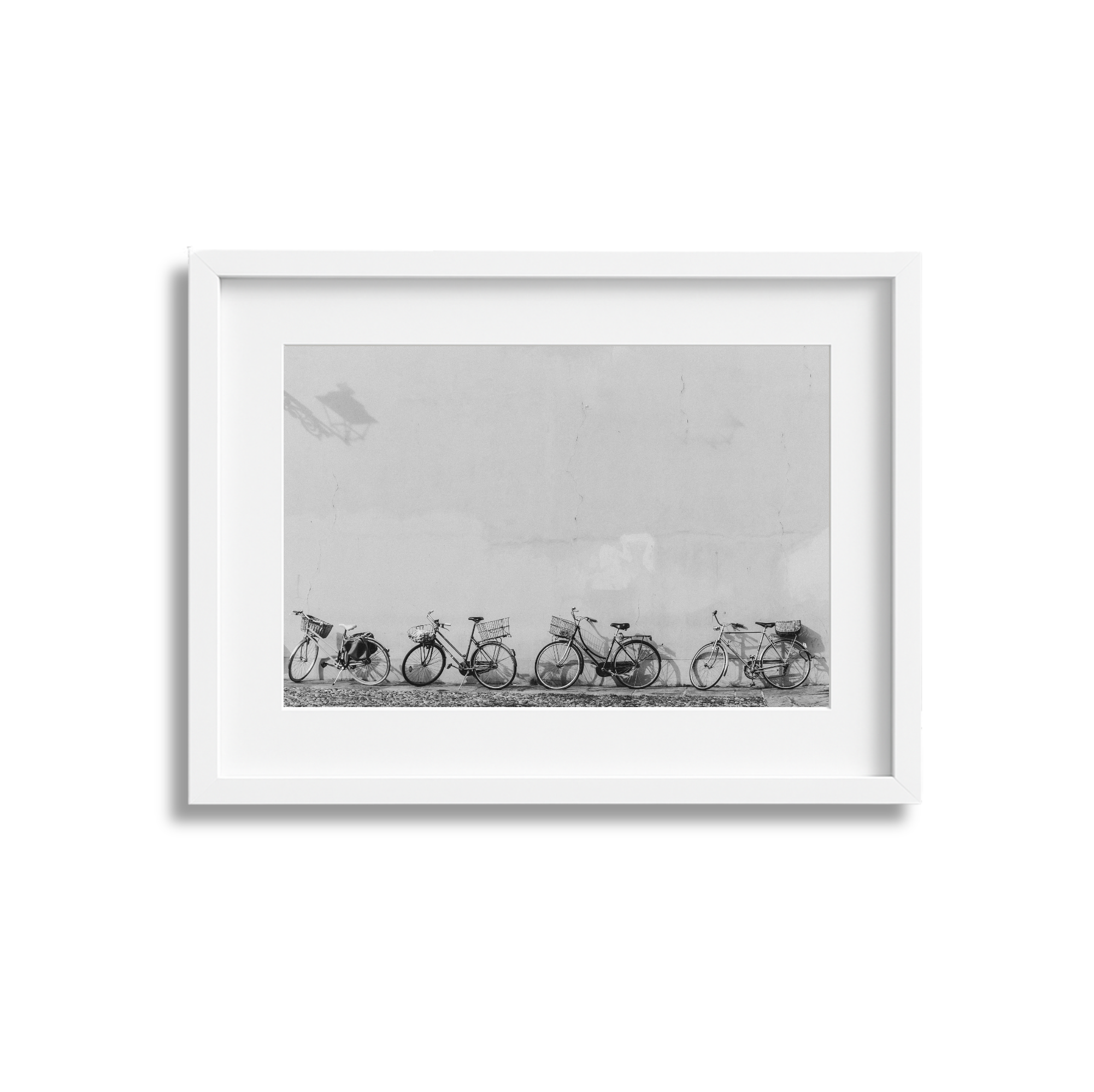 Black and white photo of five bicycles lined up against a plain wall, enclosed in a white frame.