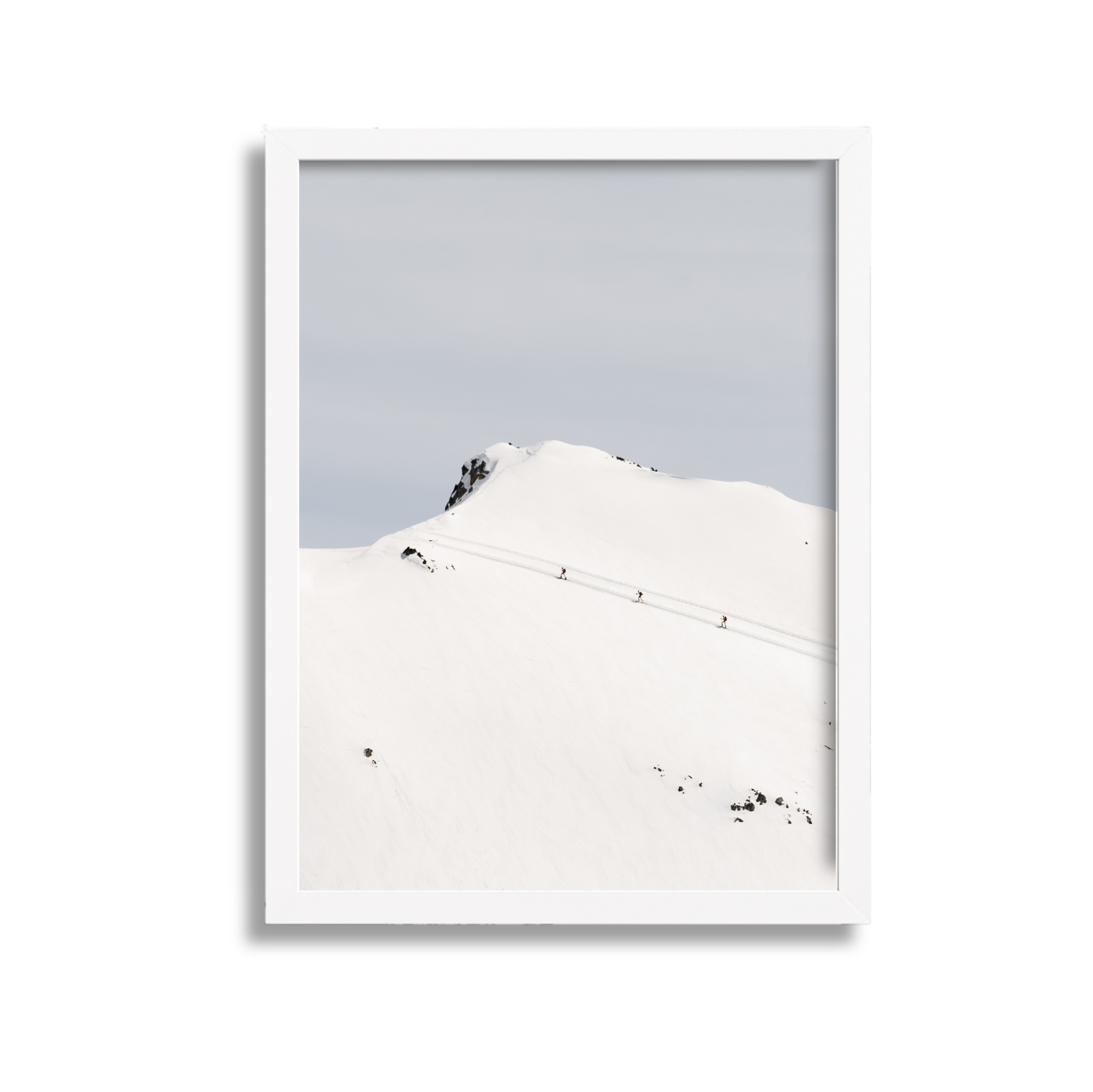 Snow-covered mountain with a few people hiking on a trail, under a cloudy sky.