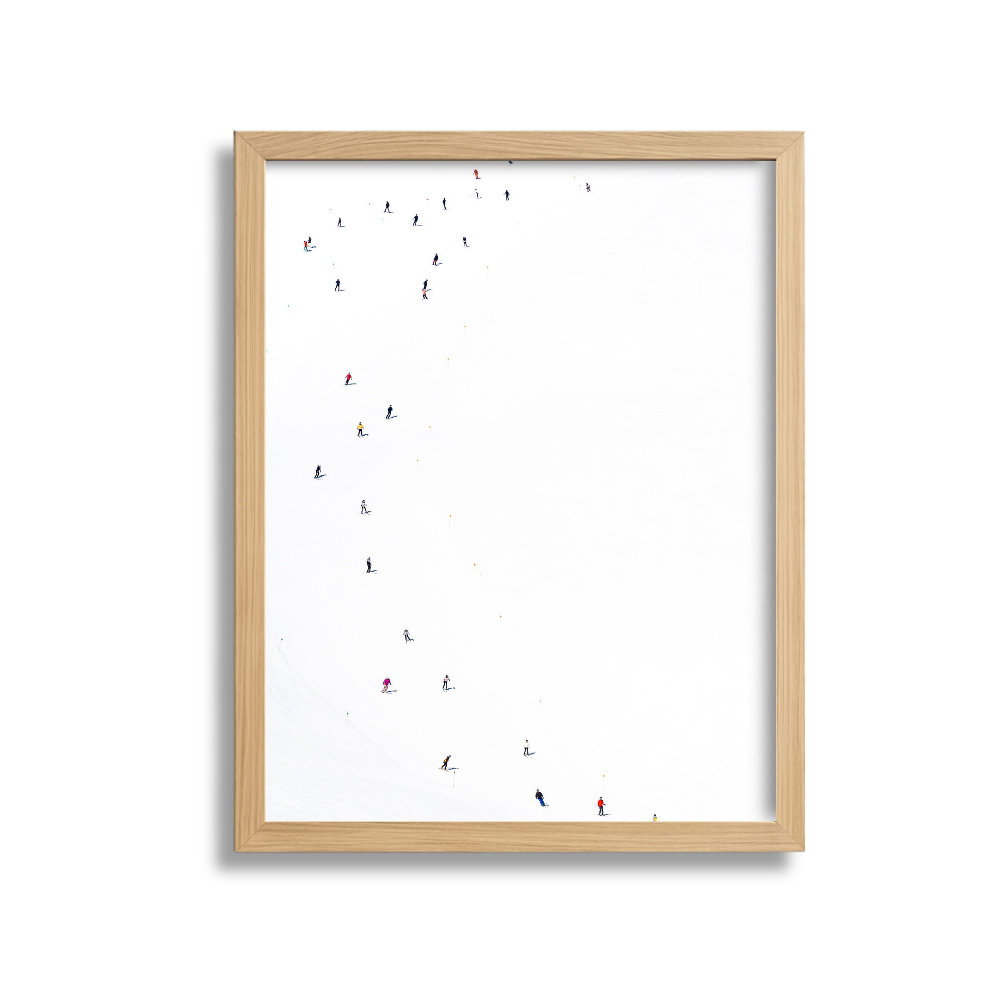 A vertical framed photograph of a snowy ski slope with multiple skiers and snowboarders scattered across the hill, viewed from above.