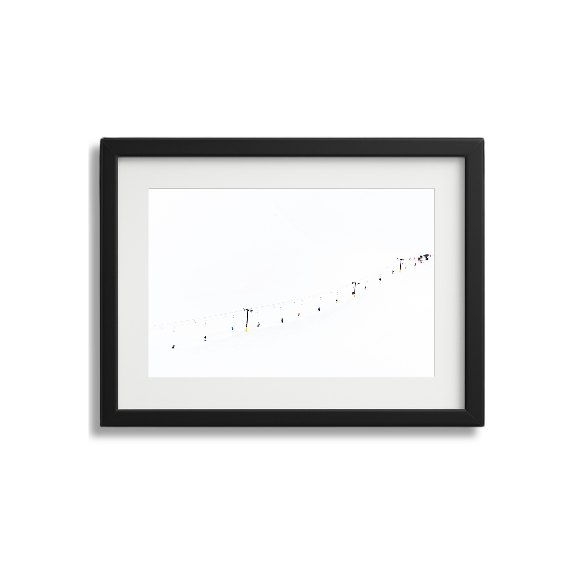 Framed photo of a snowy ski slope with colorful skiers and ski lift poles against a bright, white sky.