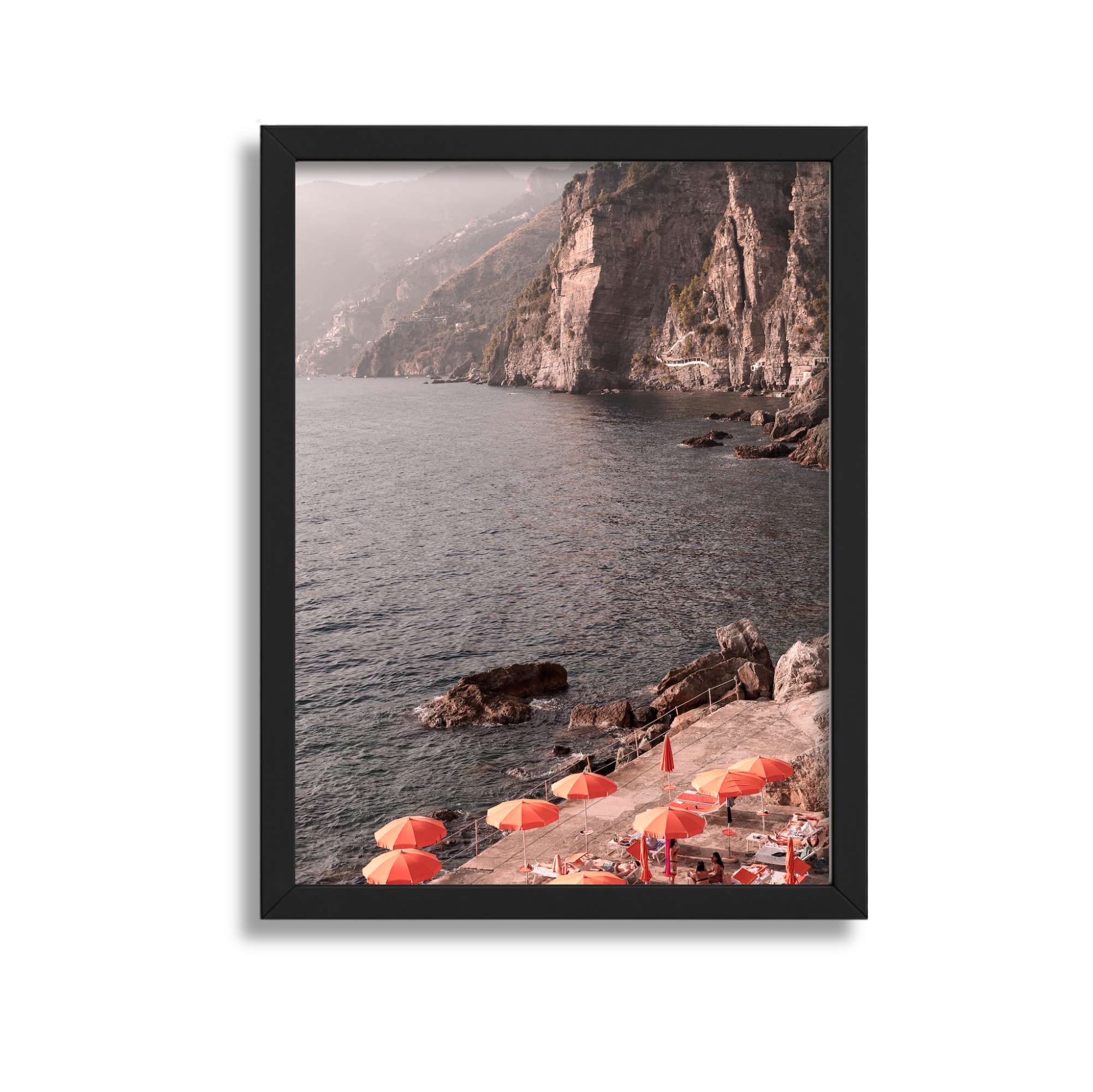 Sunset view of a rocky coastal area with cliffs and a small beach with red umbrellas and lounge chairs.