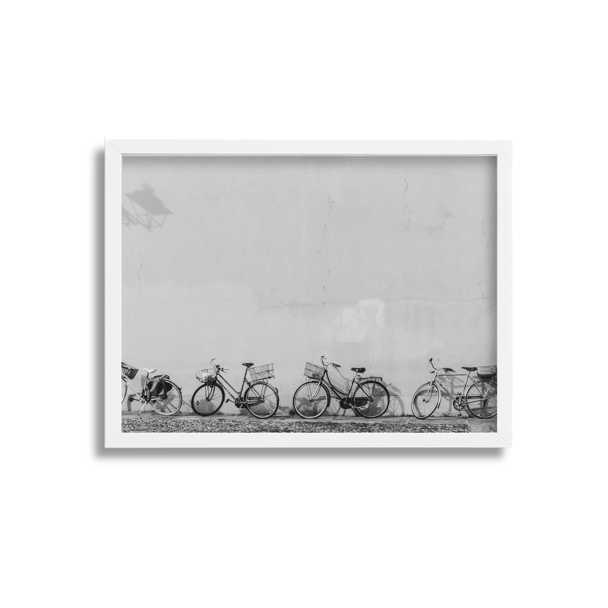 Five bicycles parked against a plain wall in black and white, with shadows cast on the wall.