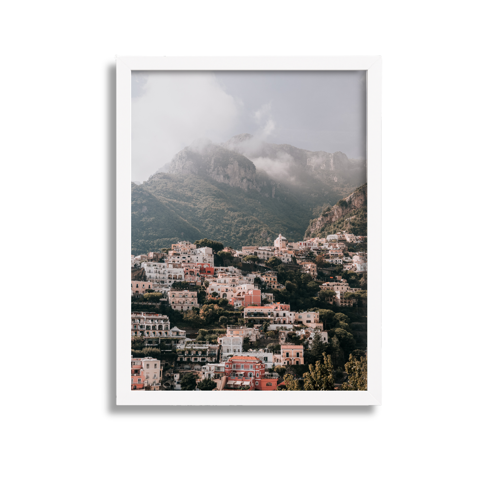 A large framed fine art photography print  scenic view of Positano Italy through a black picture frame, with mountains and cloudy sky in the background with a white frame. 