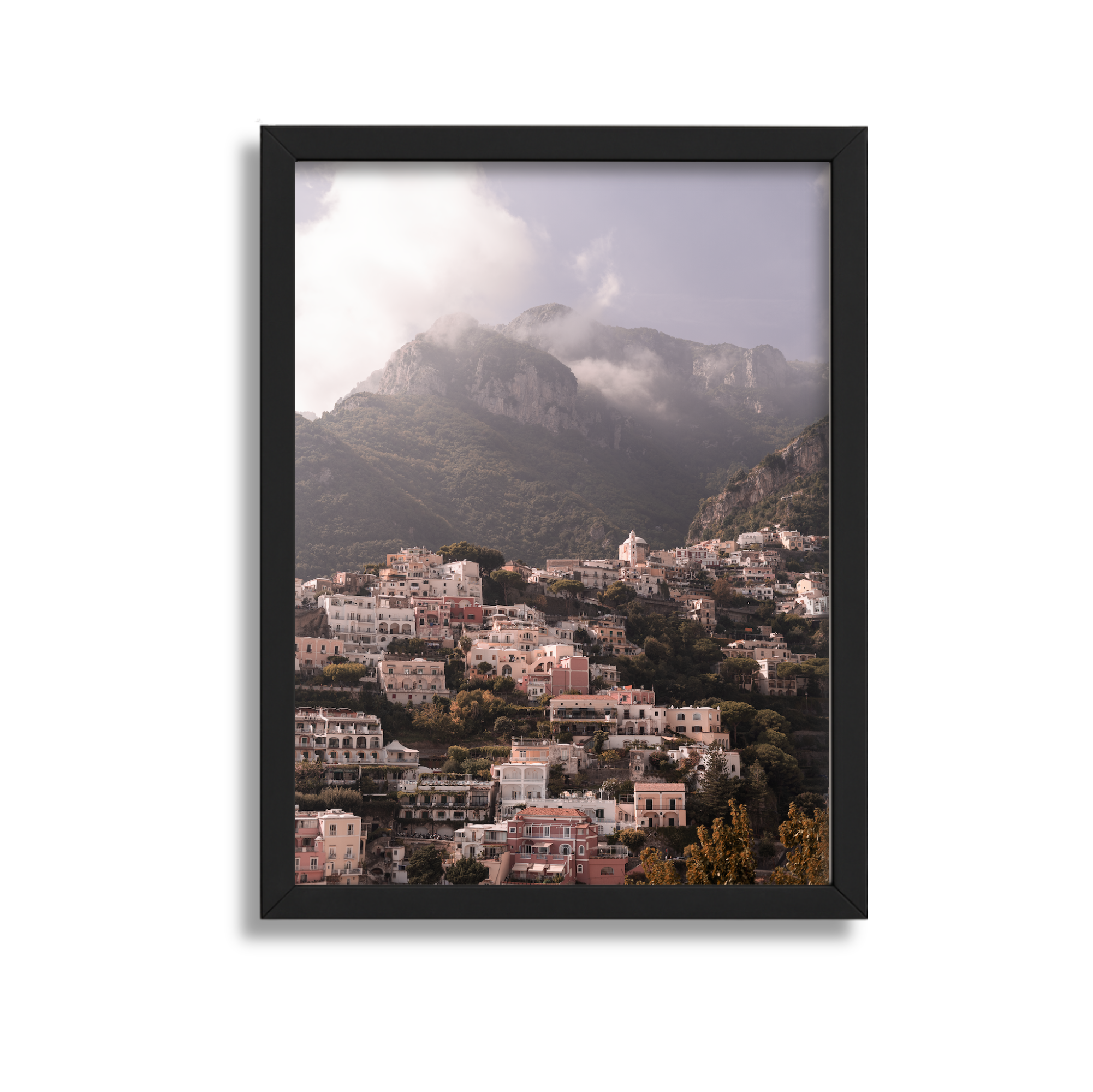 A framed photograph of a hillside town with pastel-colored buildings, overlooking mountains partly shrouded in clouds.