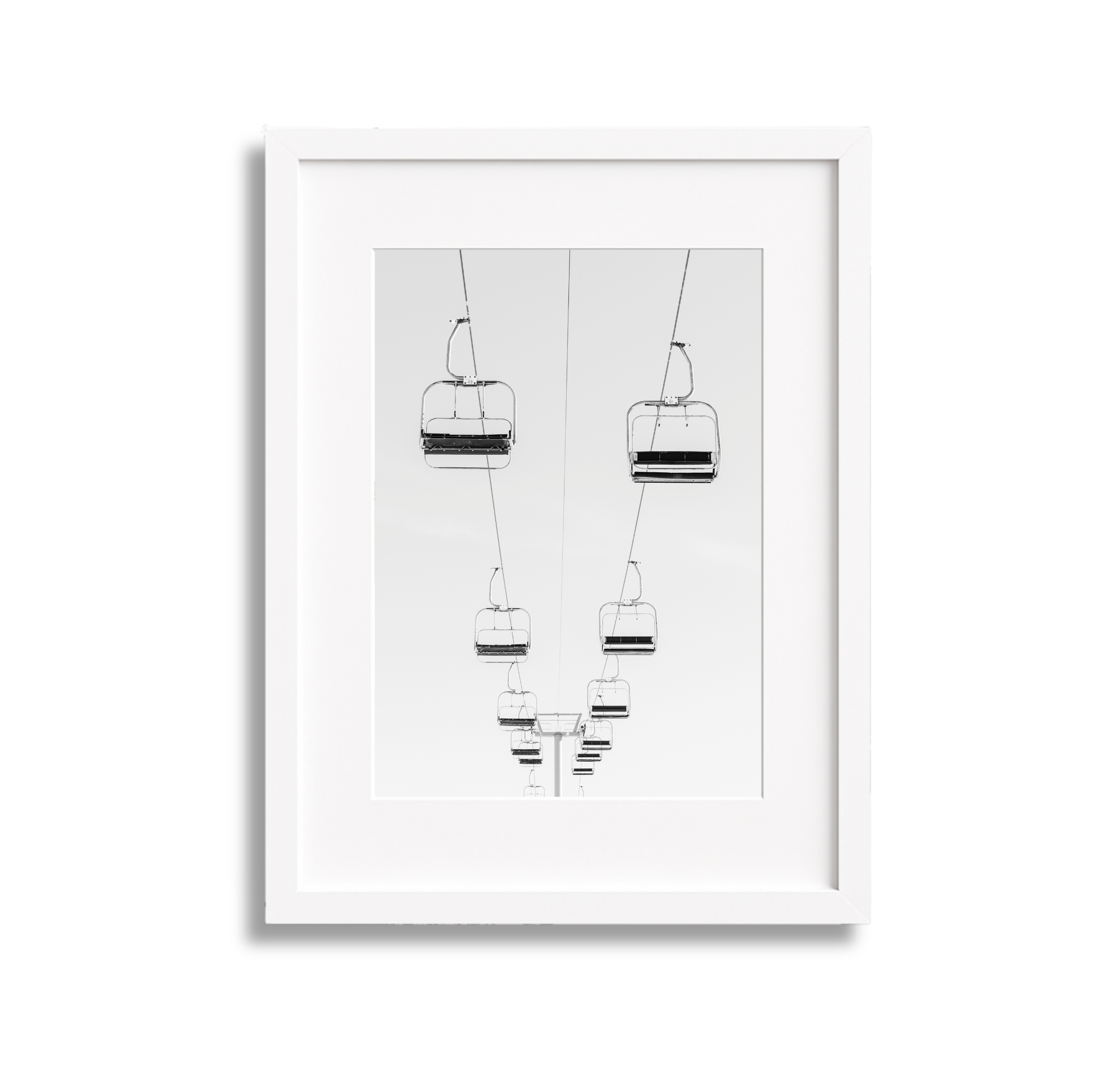 Black and white photograph of ski lift chairs suspended from cables, ascending into the distance, viewed from below.