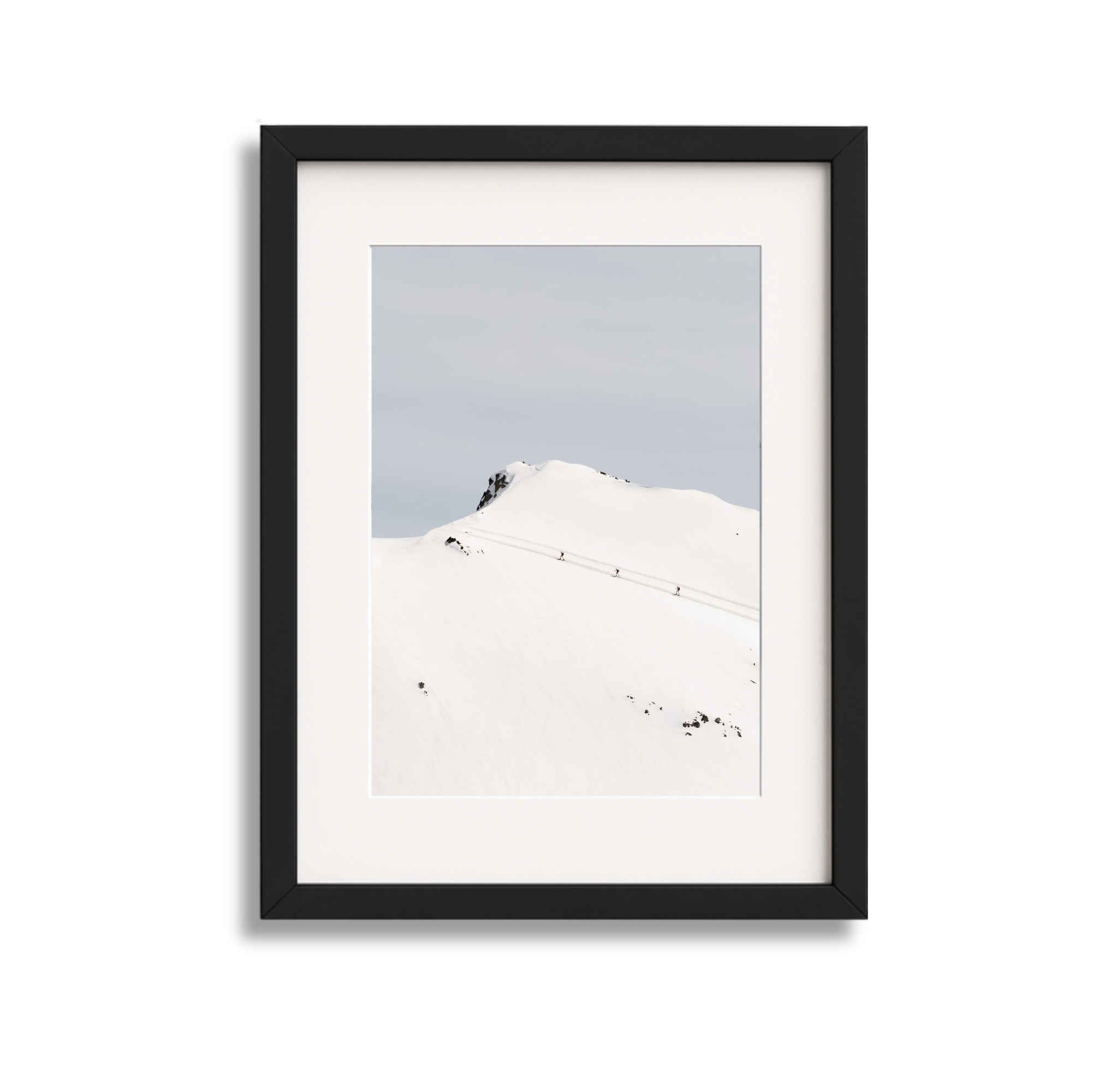 Framed photograph of snow-covered mountain with a trail of skiers ascending.