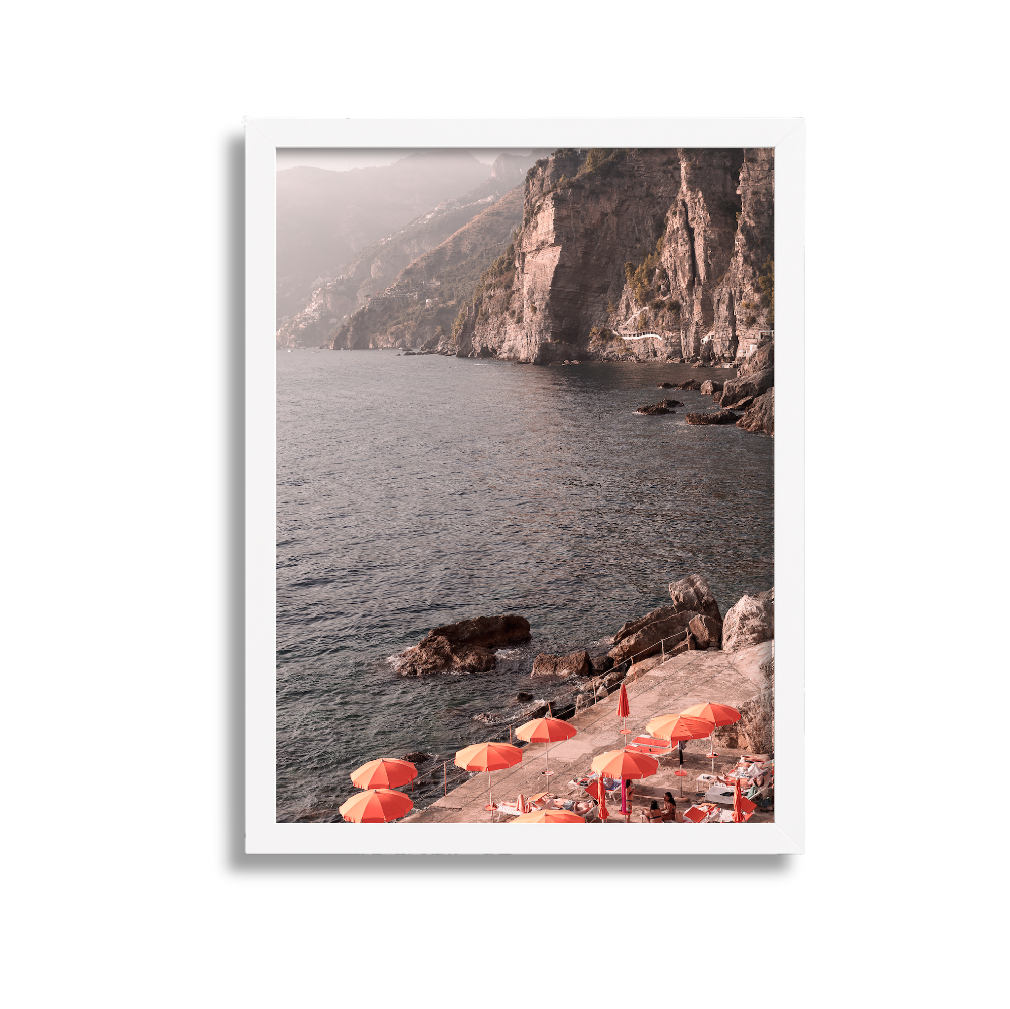 Coastal scene with orange umbrellas on a concrete pier by the sea, rocky cliffs in the background, and misty hills.