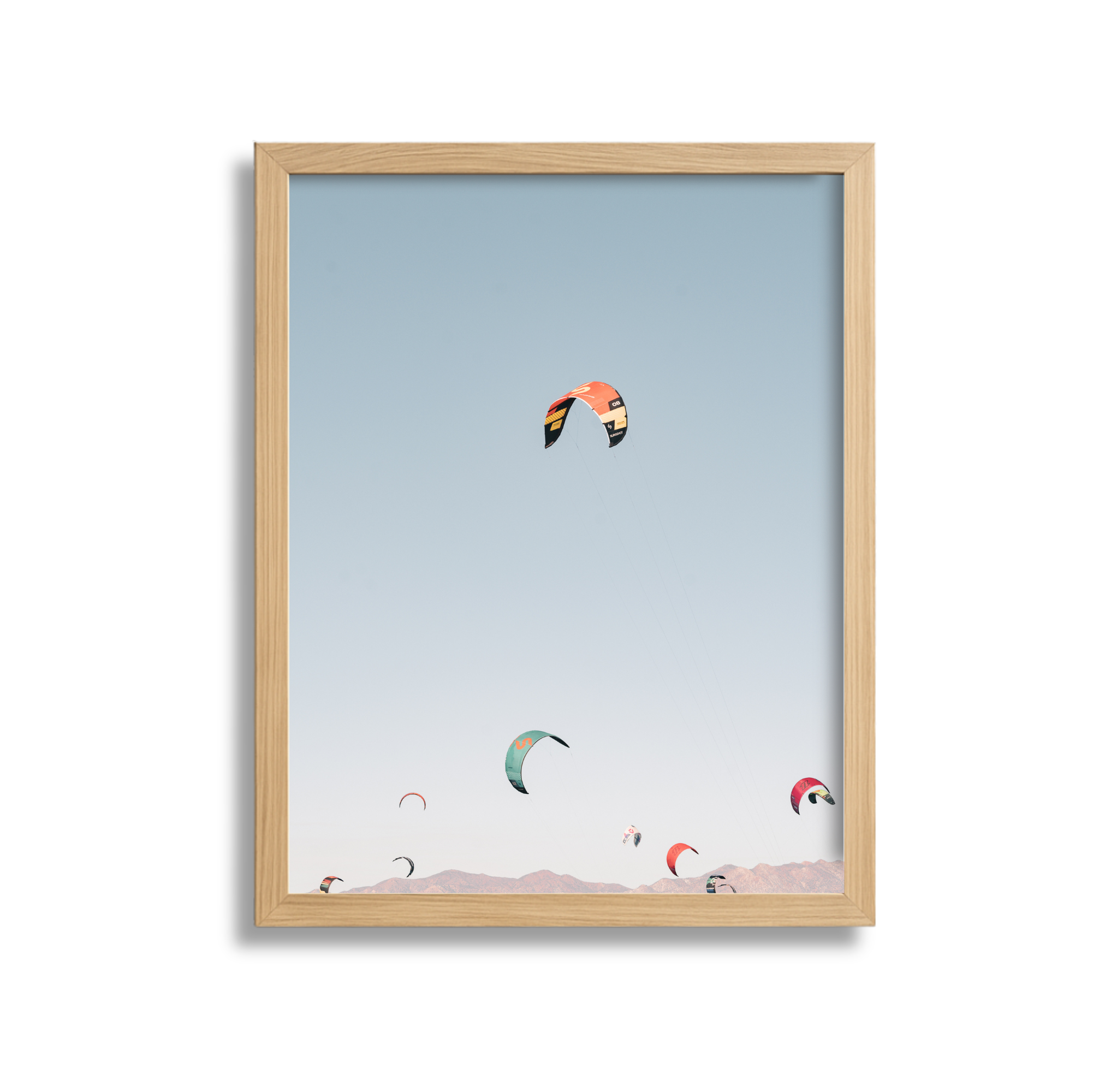 Multiple kites flying in the sky over a desert landscape with mountains in the background.