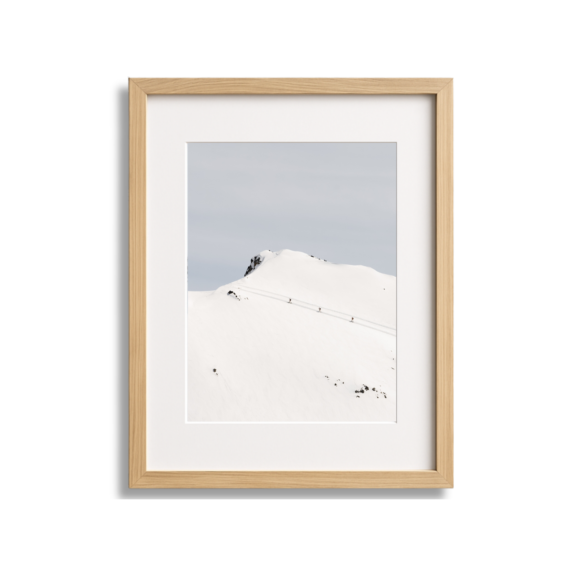 Photograph of a snow-covered mountain with a trail of skiers or hikers ascending.