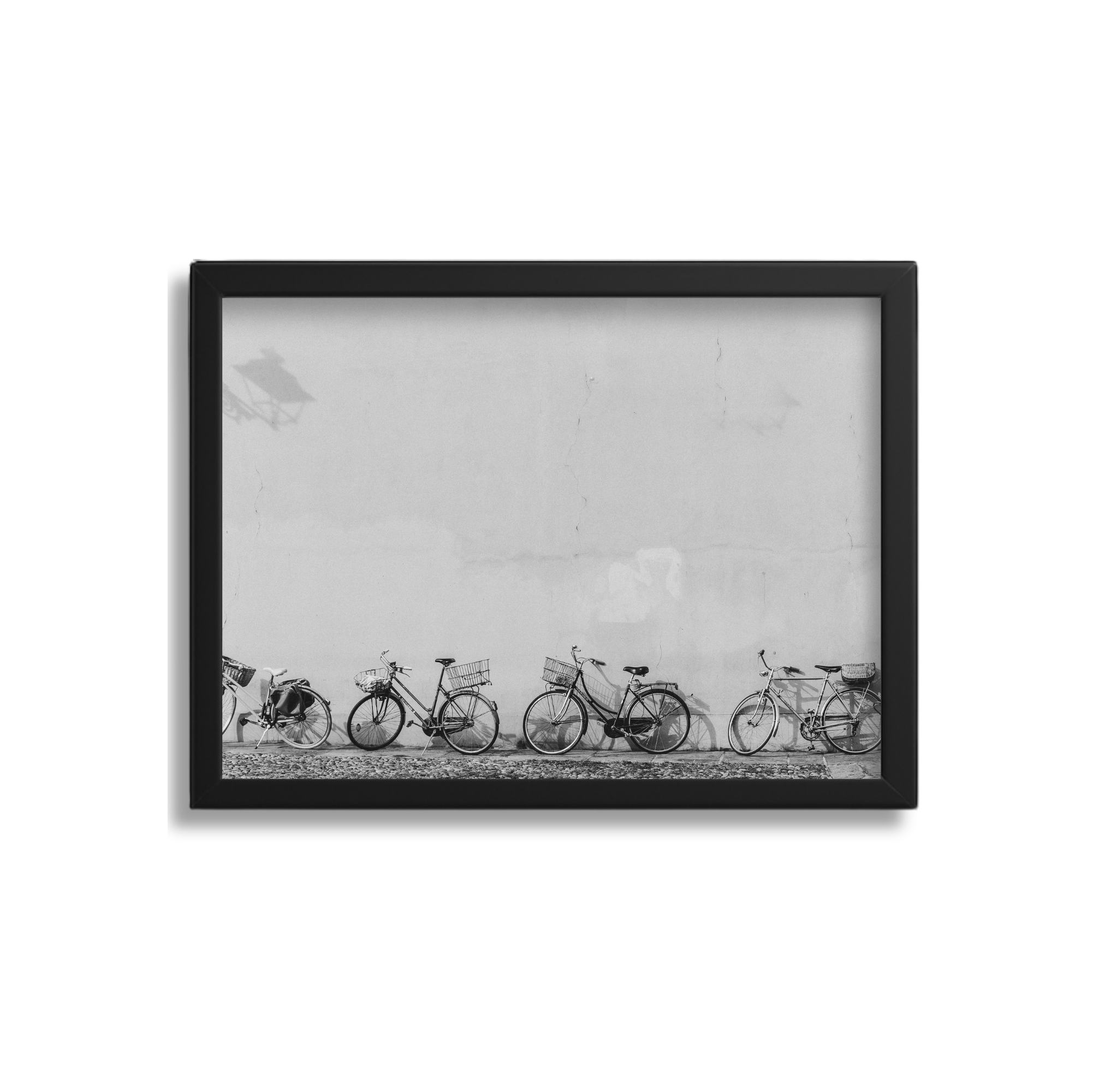 Black-framed photo of five bicycles parked against a plain wall, with faint shadows of other bicycles in the background, in black and white.
