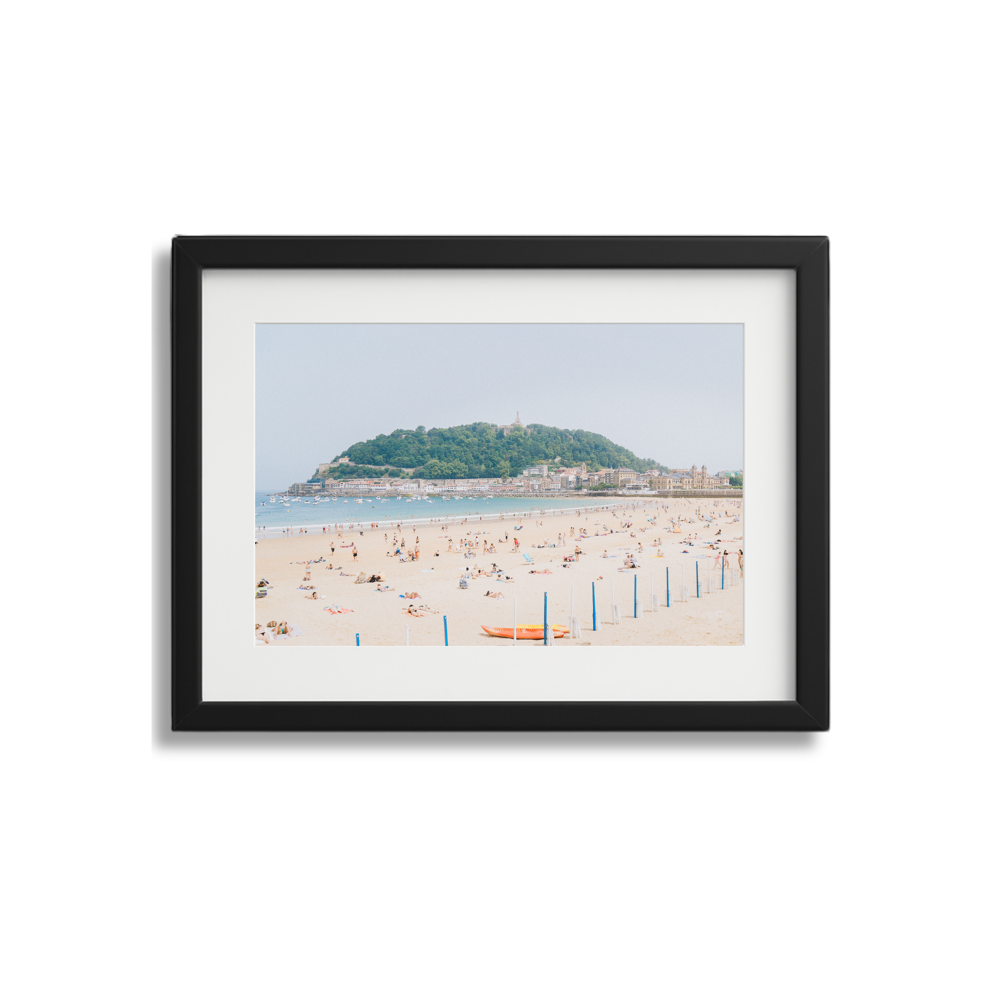 Framed photograph of a beach with people sunbathing and a hill in the background.