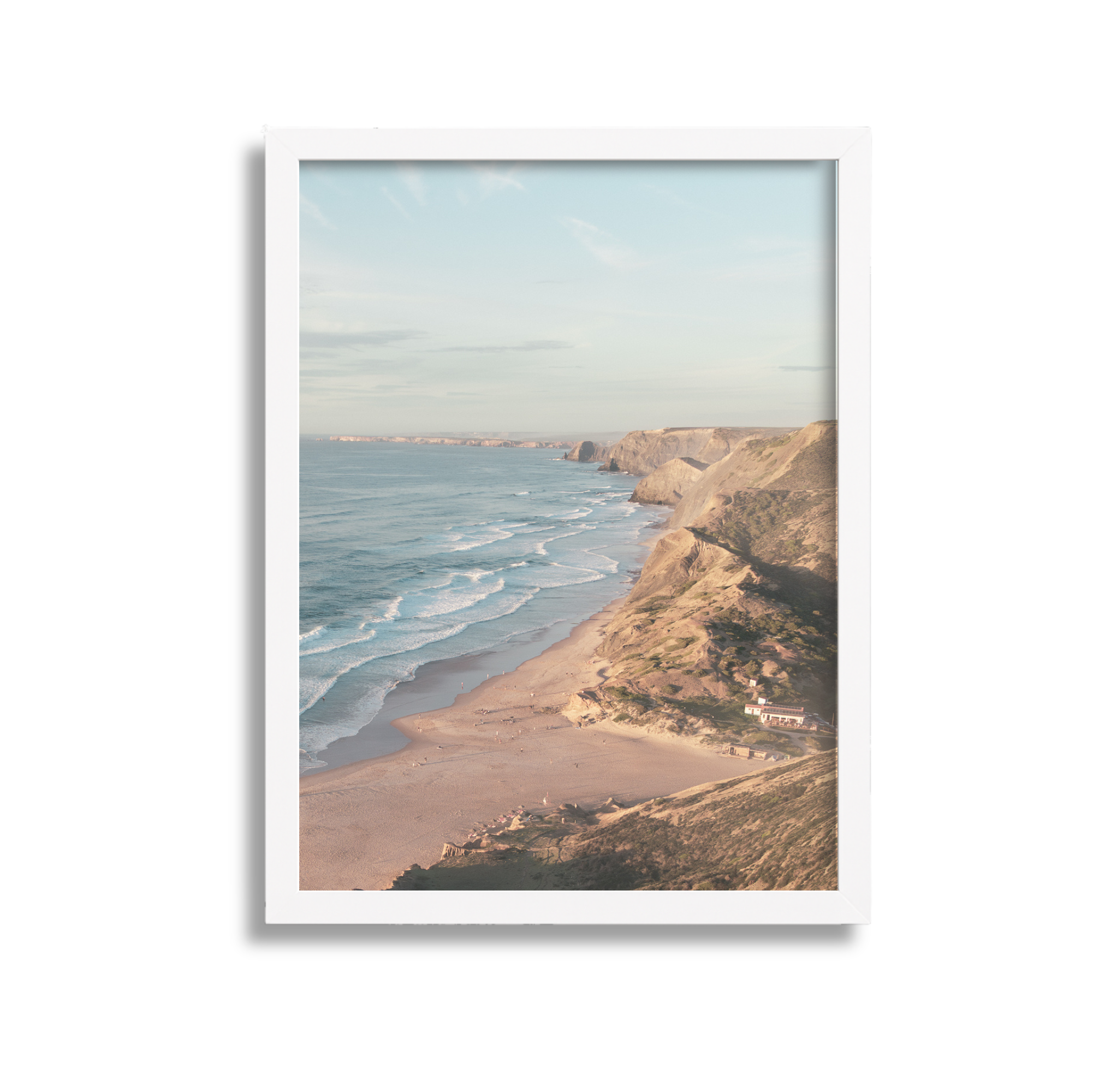 Scenic view of a beach with waves crashing on the shore, cliffs in the background, and a clear sky.