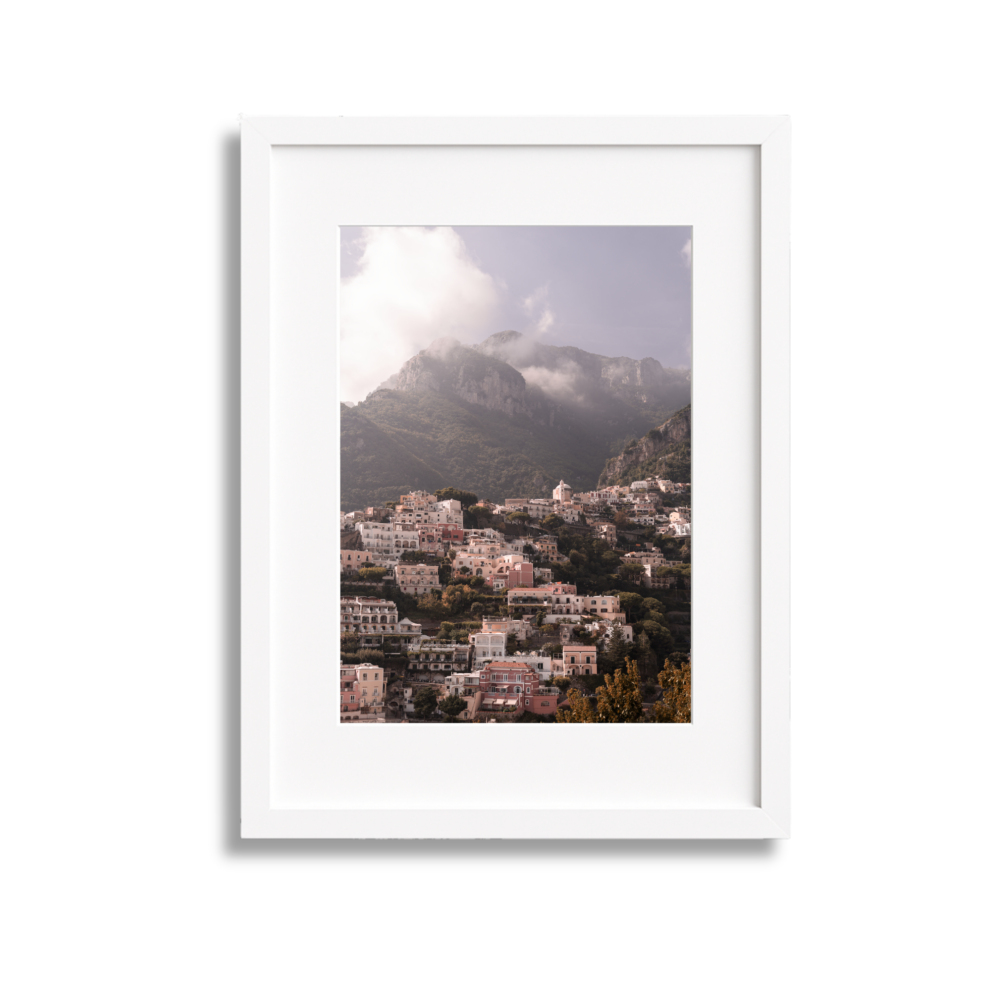 A framed photograph of a hillside town with many white buildings, mountains in the background, and clouds partially covering the mountain peaks.