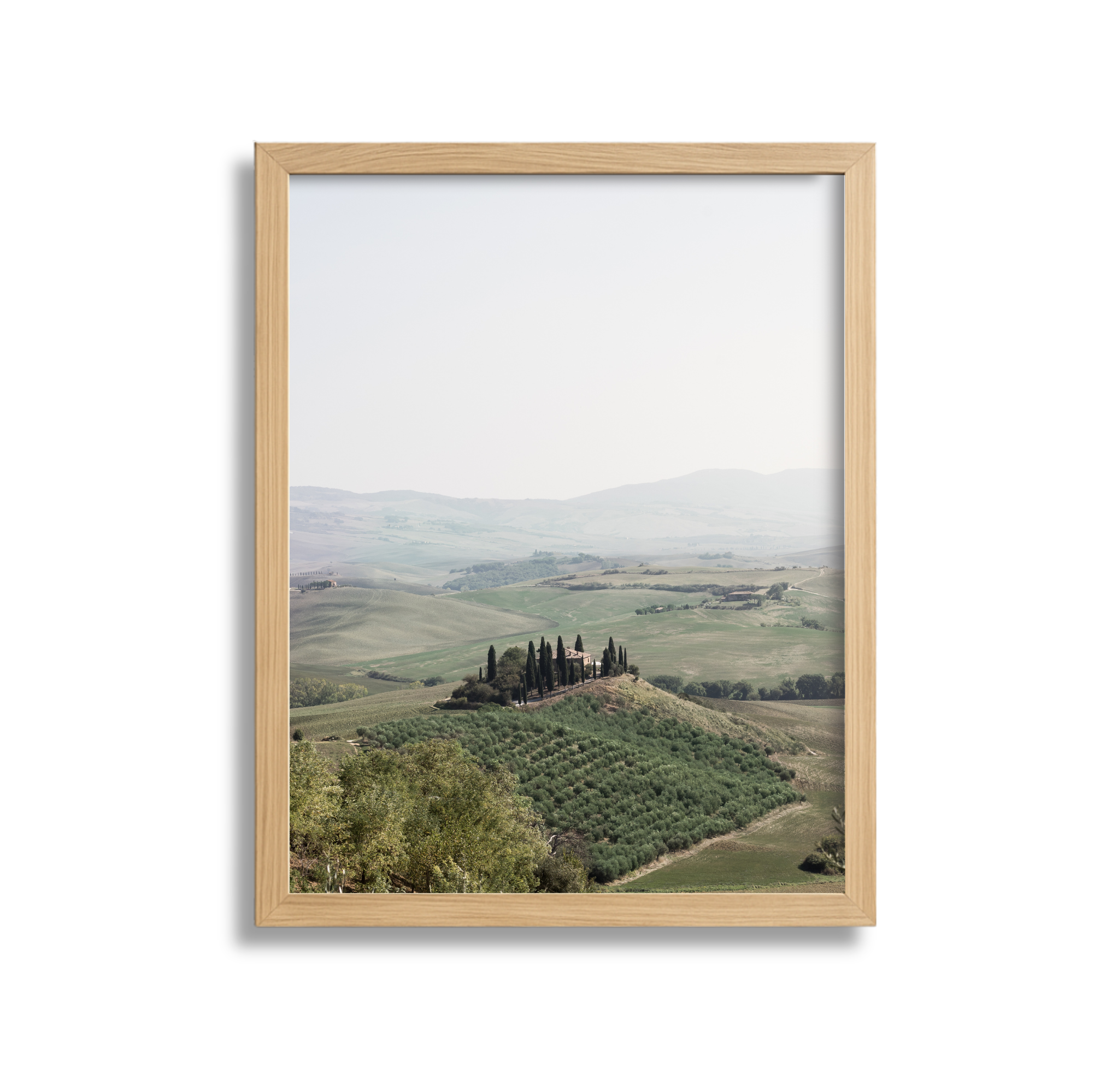 Landscape view of rolling hills with a central cypress-lined estate, framed by a wooden picture frame.