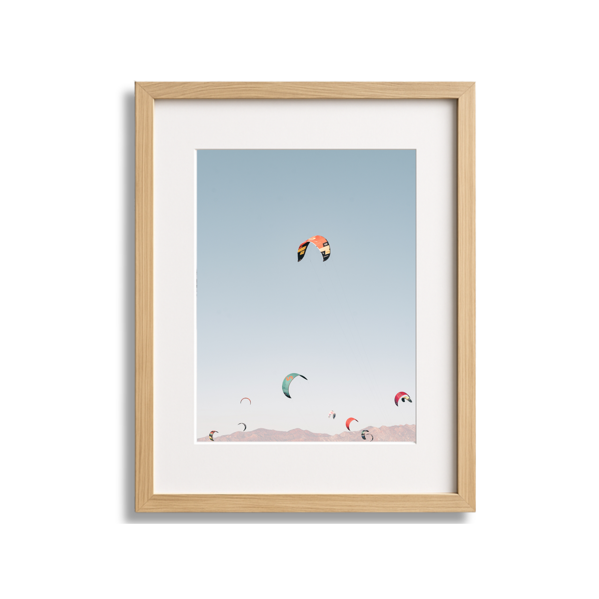 Framed photo of multiple colorful kites flying in the sky over mountains.