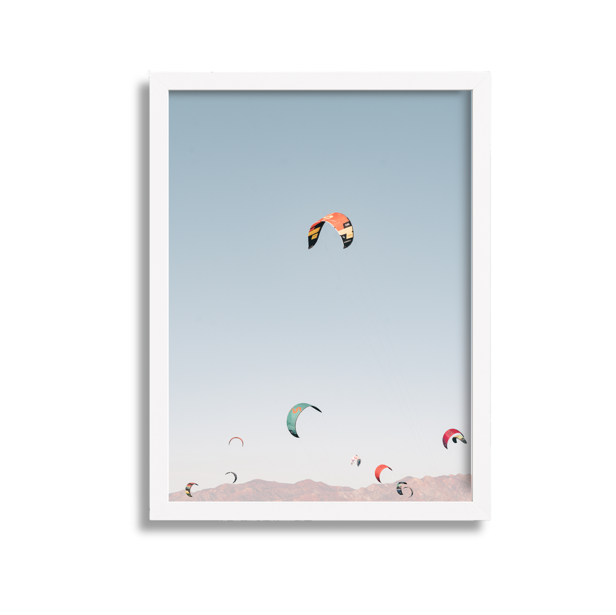 Multiple colorful kites flying in a clear sky above mountains.