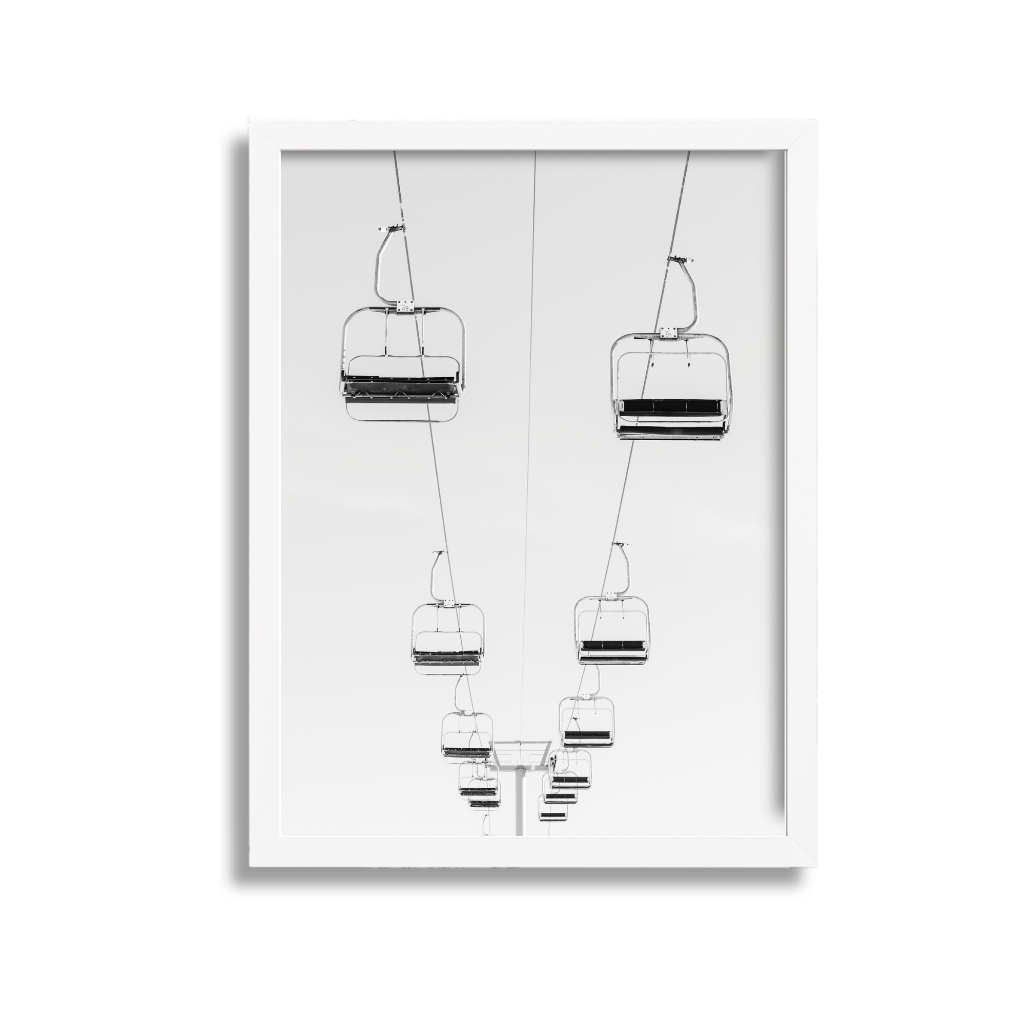 Black and white photograph of a ski lift with chairs suspended in the air against a clear sky.