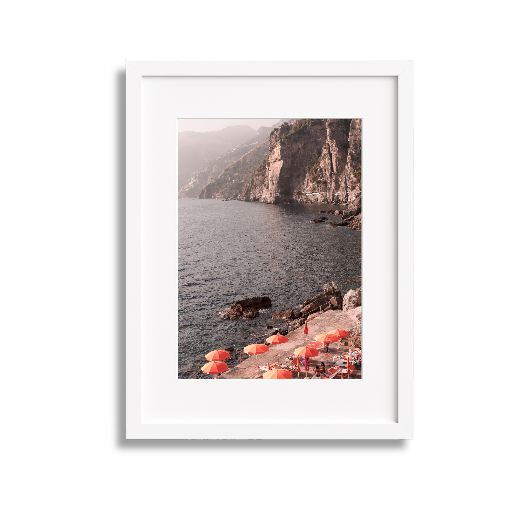 Photograph of a lakeside scene with orange umbrellas and lounge chairs, rocky shoreline, cliffs in the background, and mountains under a hazy sky.
