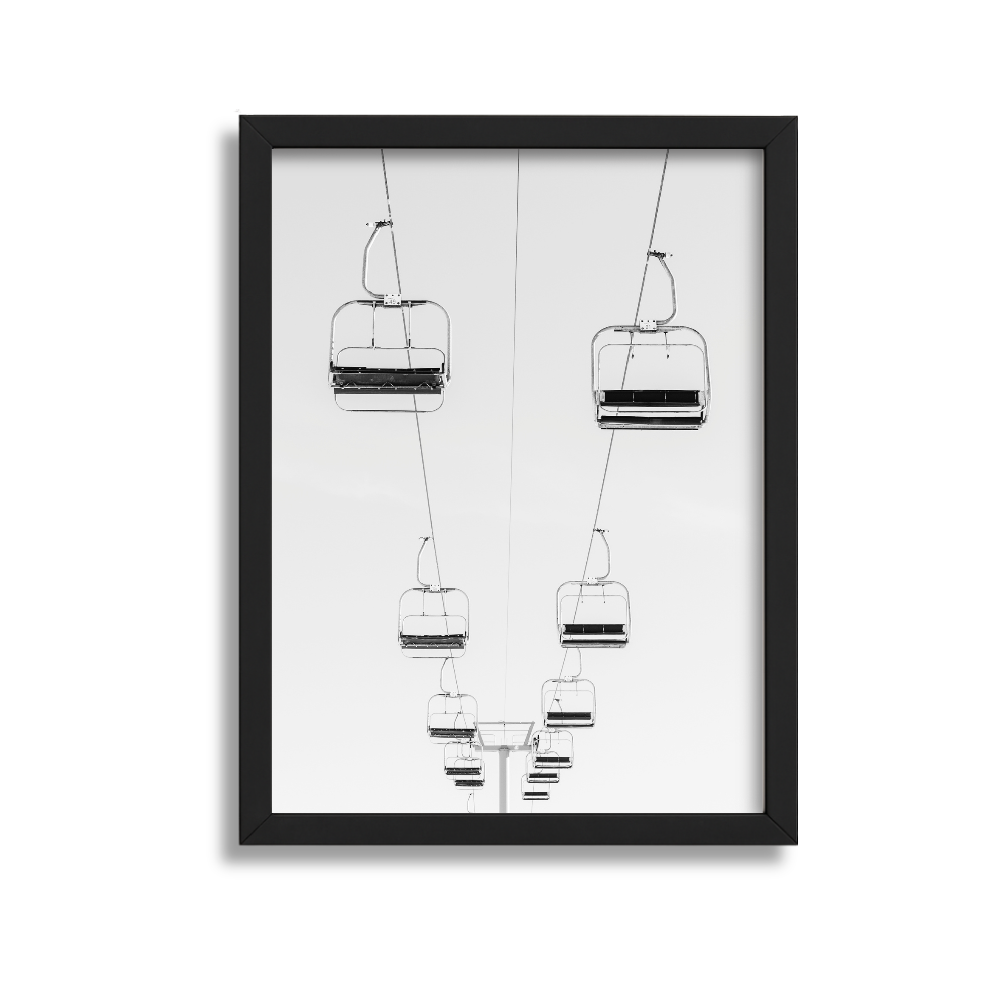 Black and white photograph of empty ski lift chairs suspended in the air against a clear sky, seen from below.