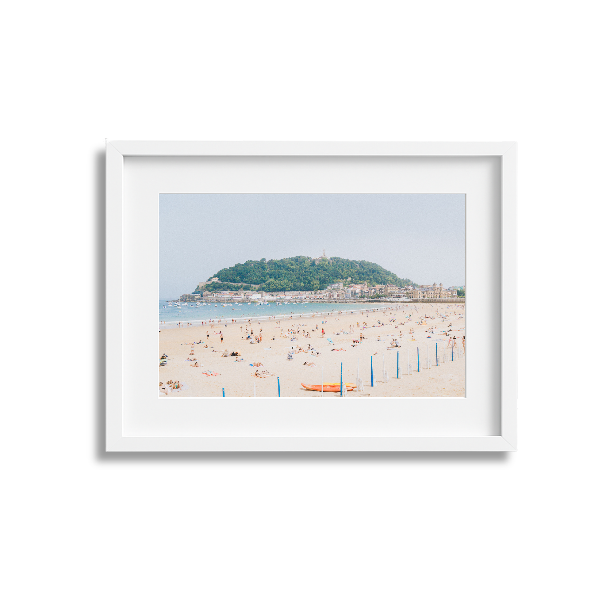 Photograph of a beach with people sunbathing, swimming, and relaxing, with a hill in the background.