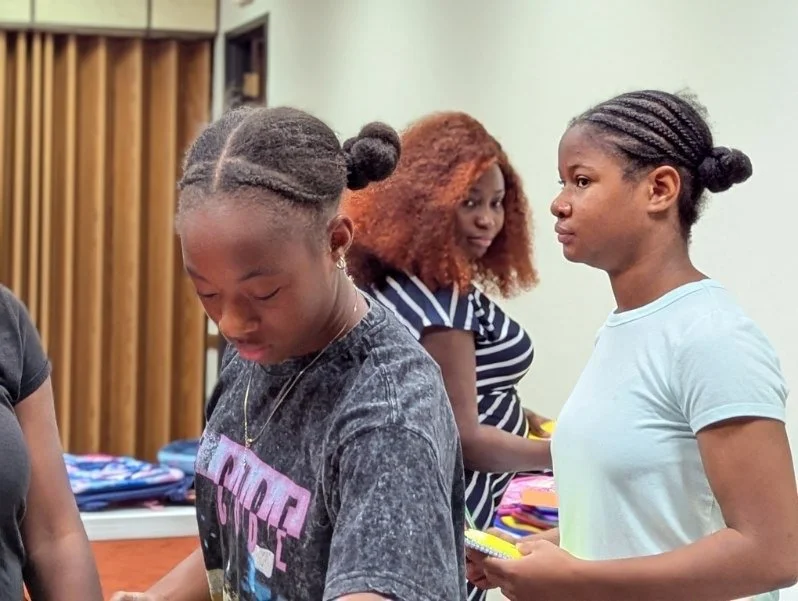 Three young girls with braided hair standing in a room, one with braids tied in a bun, another with curly hair, and a third with a ponytail, all engaged in an activity.