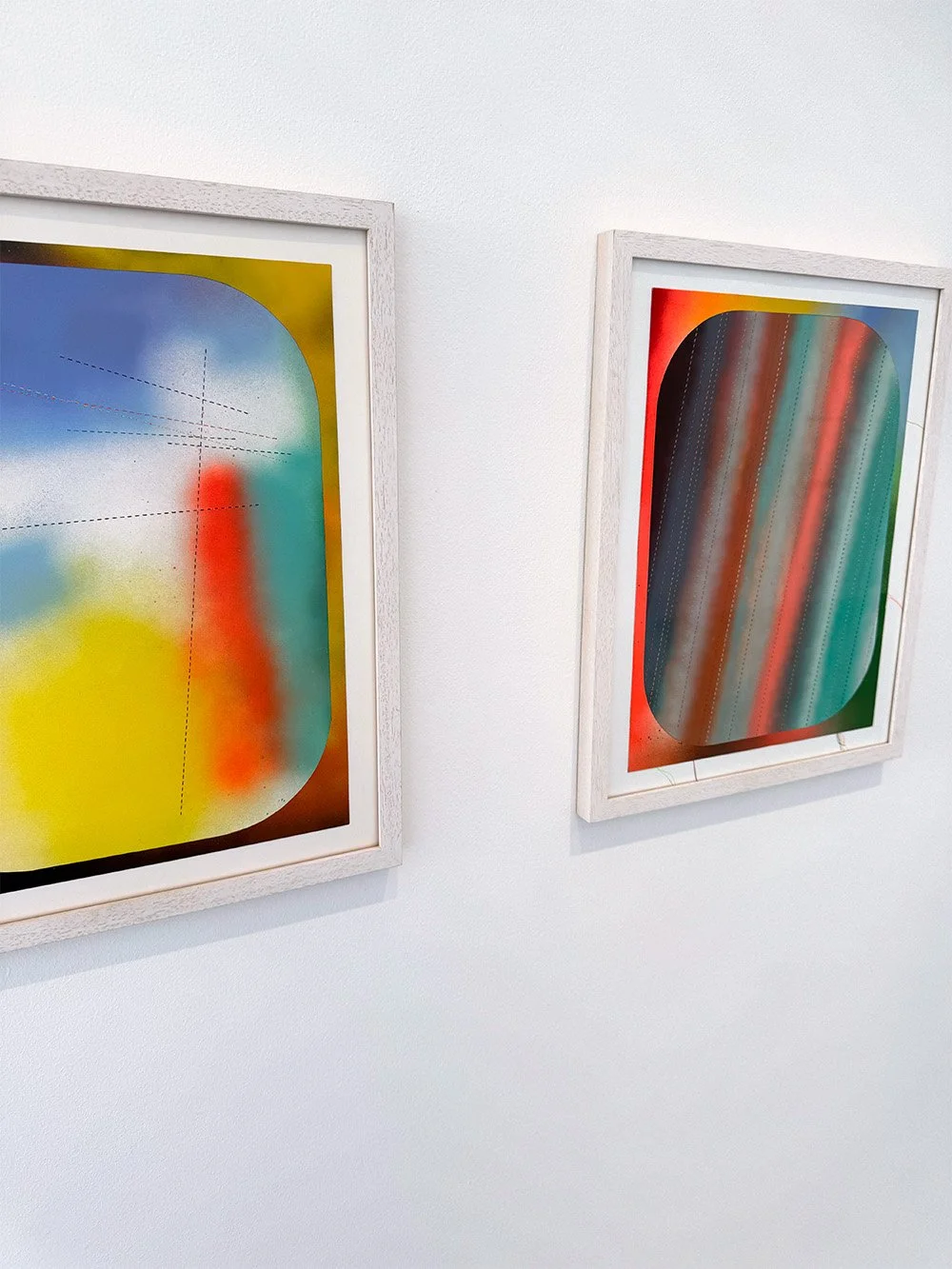 Two contemporary artworks on a white gallery wall by artist Dan Devening. The work is framed in white and made up of multi color spray enamel.