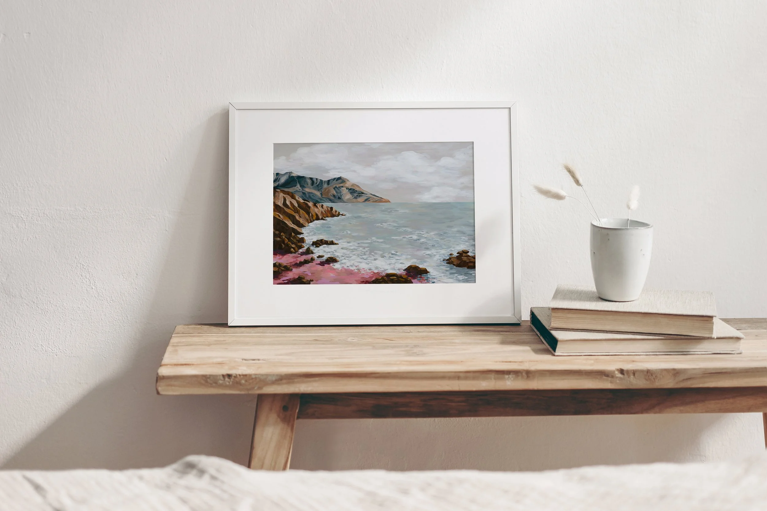 Yellow, Pink, and Blue Ocean and Mountain Painting framed on a wooden desk