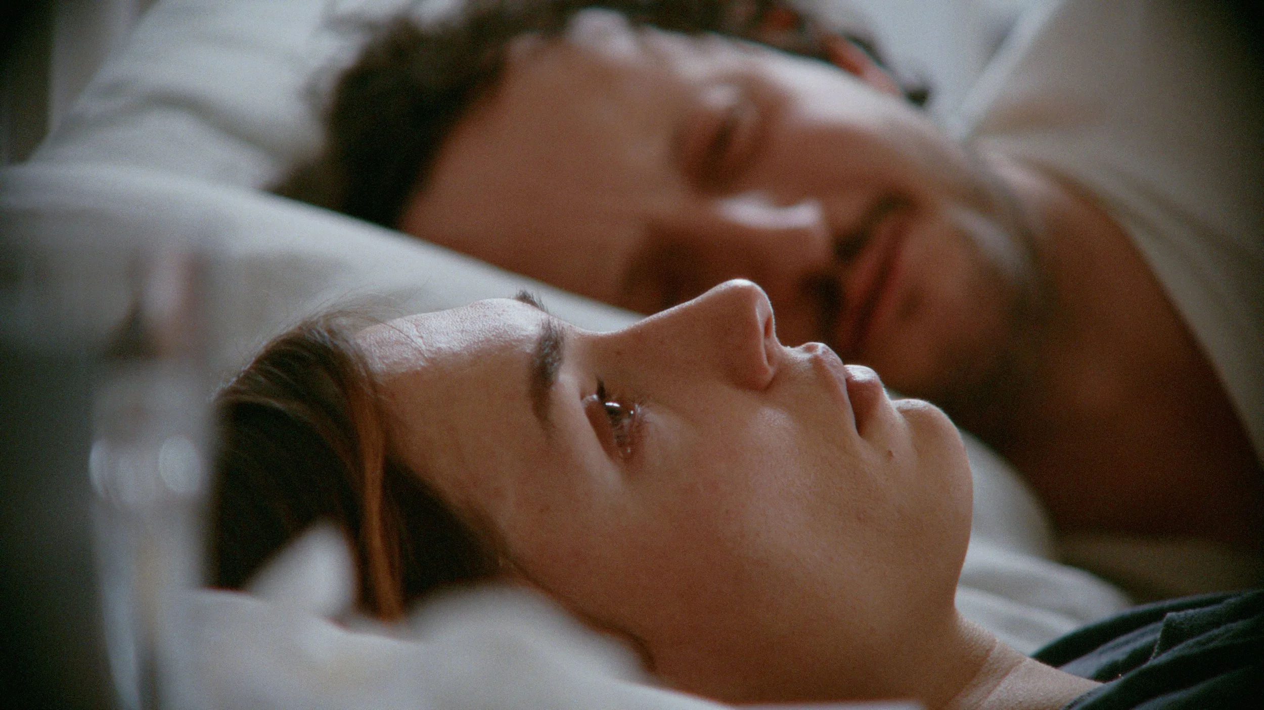 Profile of woman lying in bed as a man lies next to her, vintage 90s 35mm film stock emulation colors