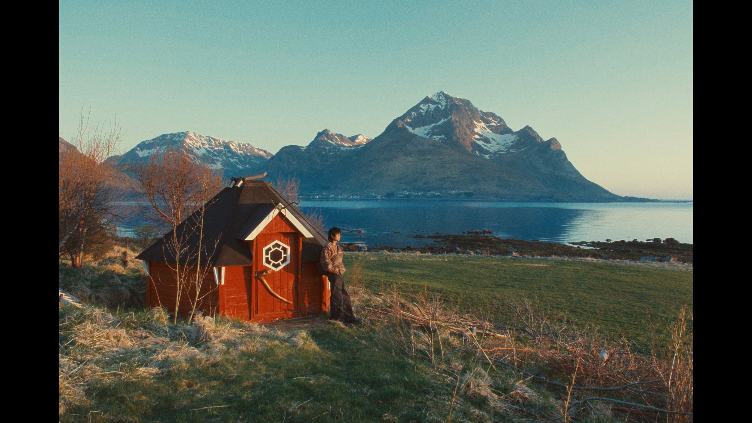 Man posing with red house in front of mountain