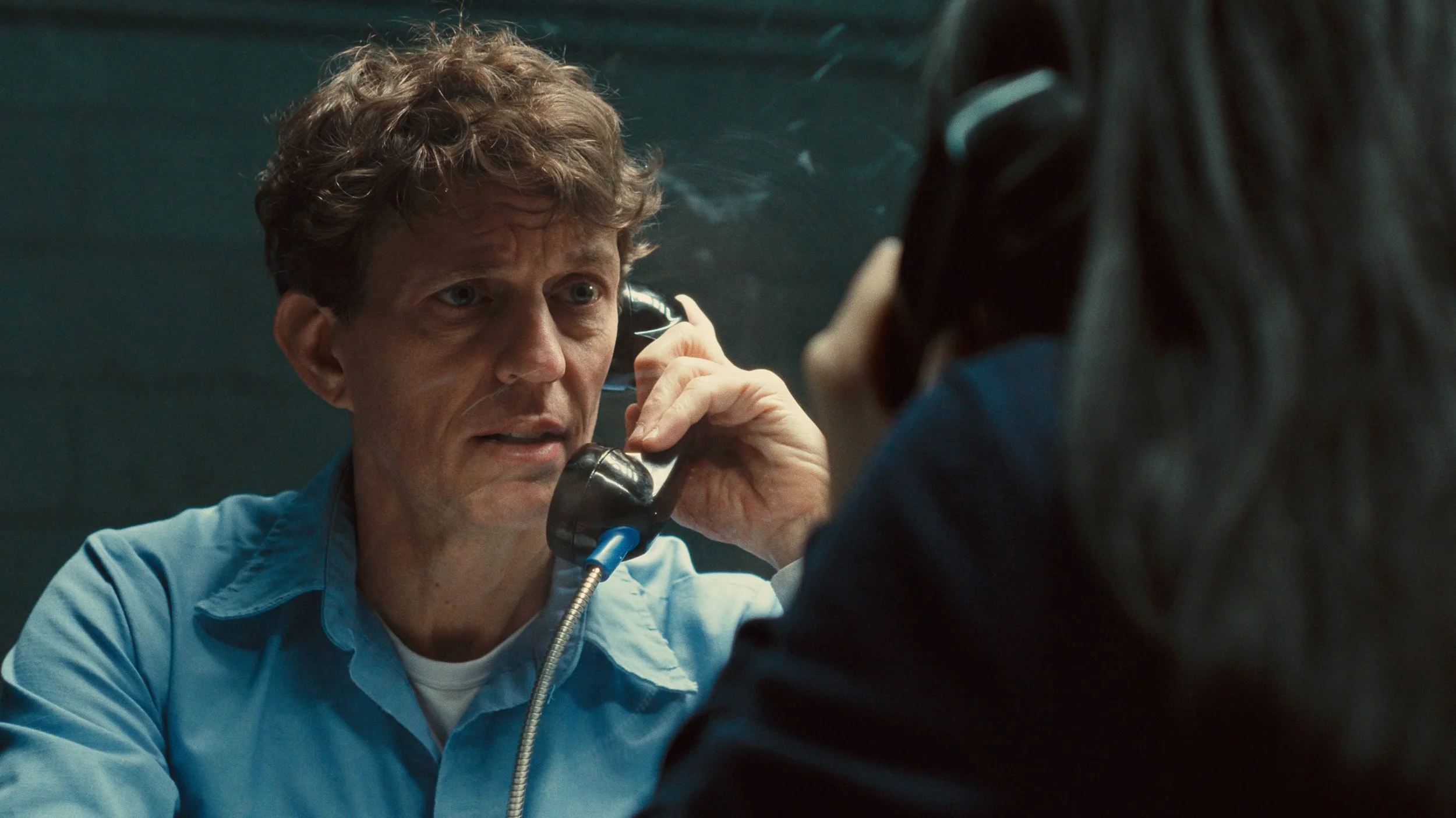 Man talking on phone in prison visitation with steely blue film color grade