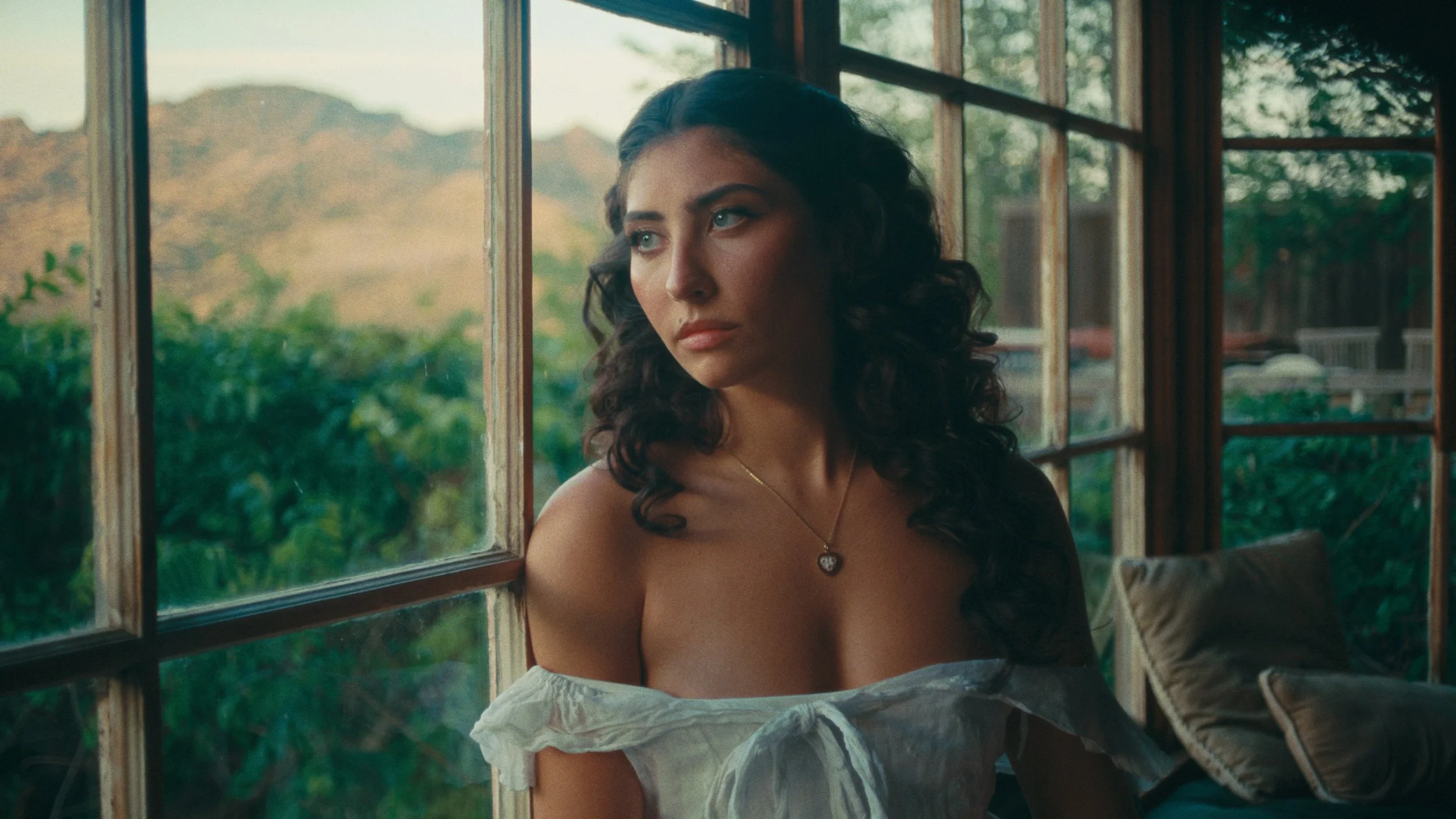 Woman in white dress sitting by window with soft cinematic light color graded with kodak print film 2383 LUT
