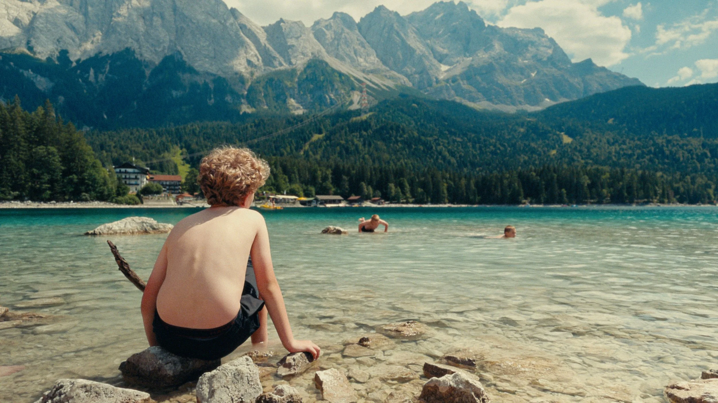 Boy sitting at the edge of a blue mountain lake in Germany, color graded with kodak print film emulation 