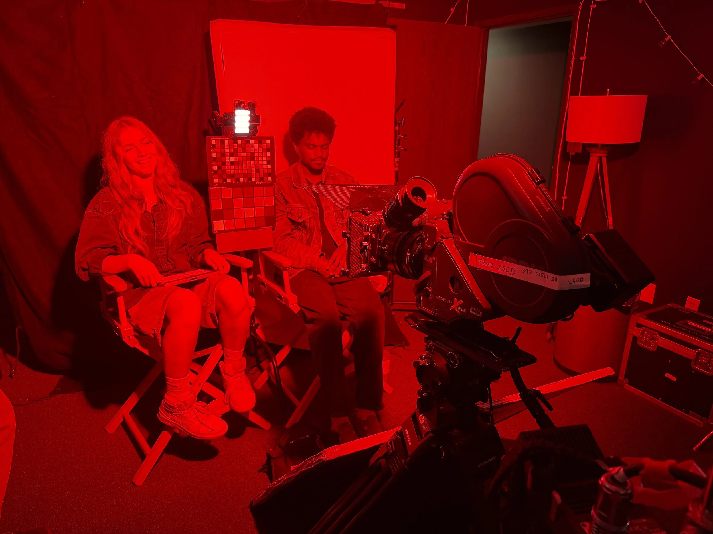 man and woman sitting in front of film camera in red lighting for film emulation color test