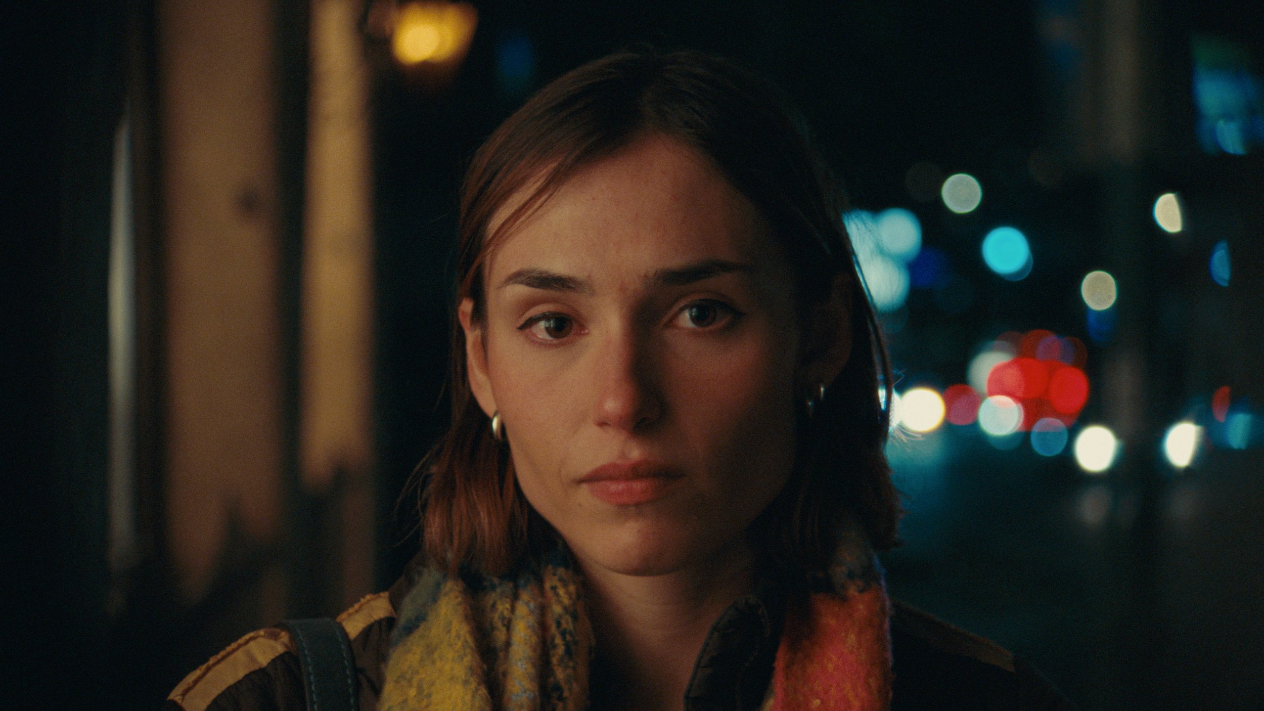 Portrait of young woman at night with glowing lights in the background, colored with 16mm kodak 500T film emulation