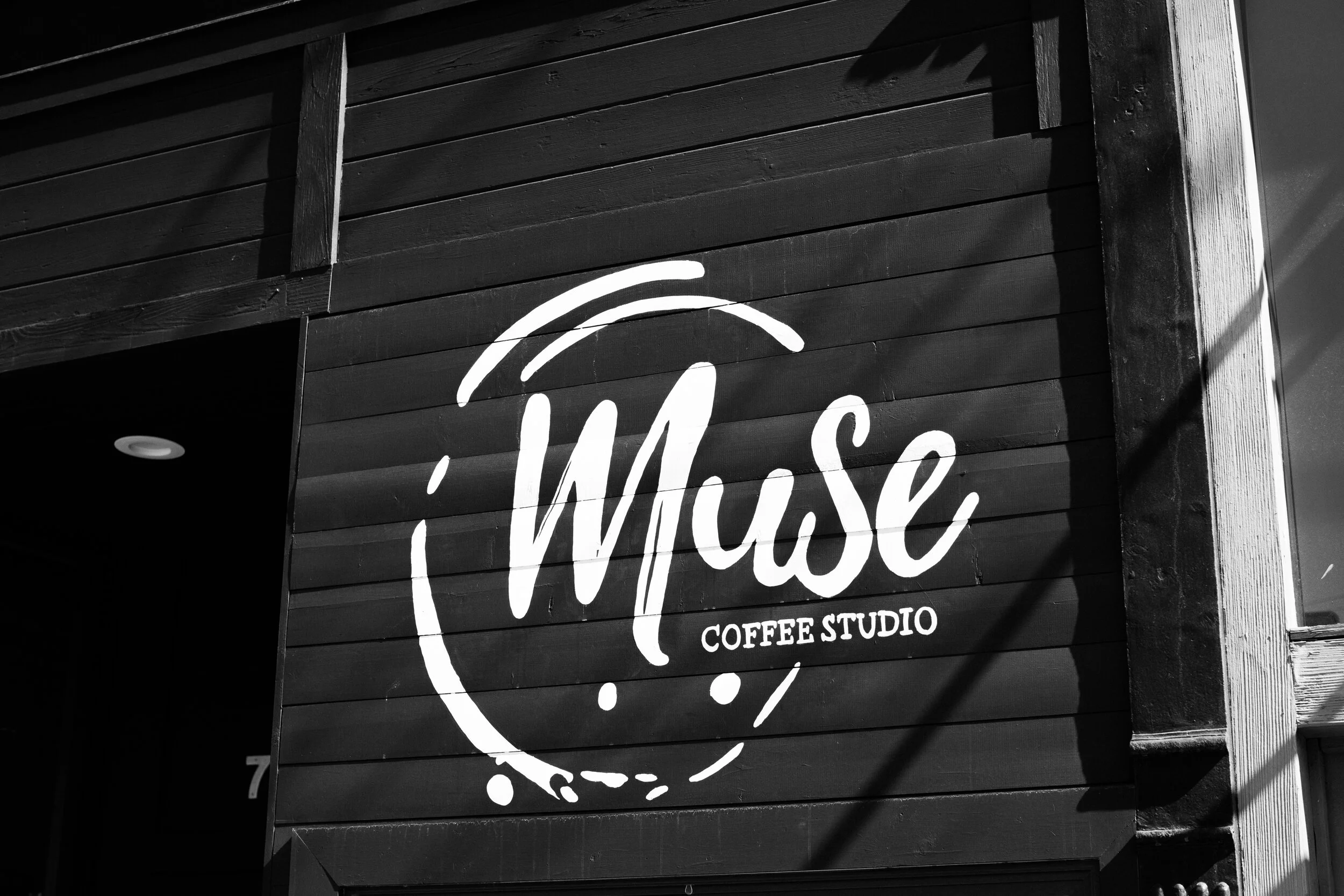 Close-up of a black wooden wall with a white handwritten-style sign that reads 'Willow Coffee Studio' and a stylized coffee cup graphic.