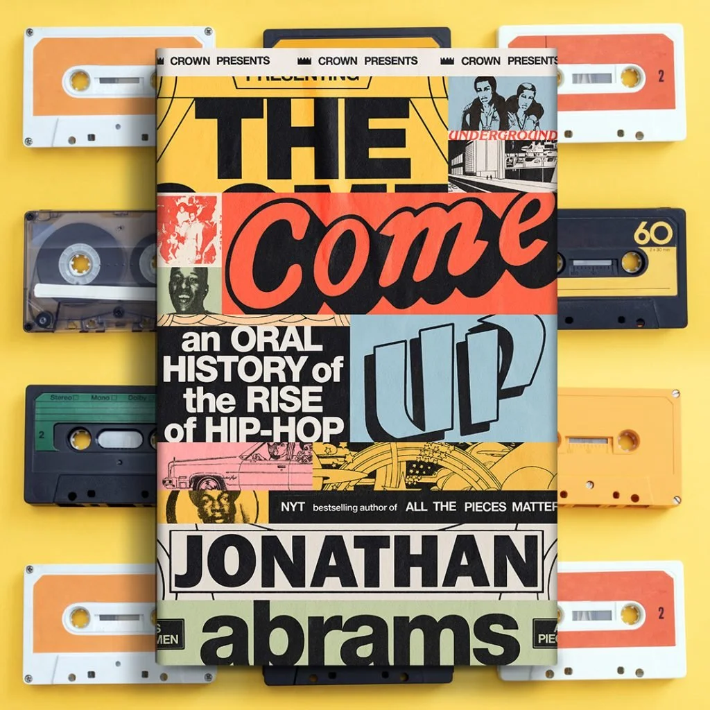 Book titled 'The Come Up: An Oral History of the Rise of Hip-Hop' by Jonathan Abrams, surrounded by vintage cassette tapes on a yellow background.